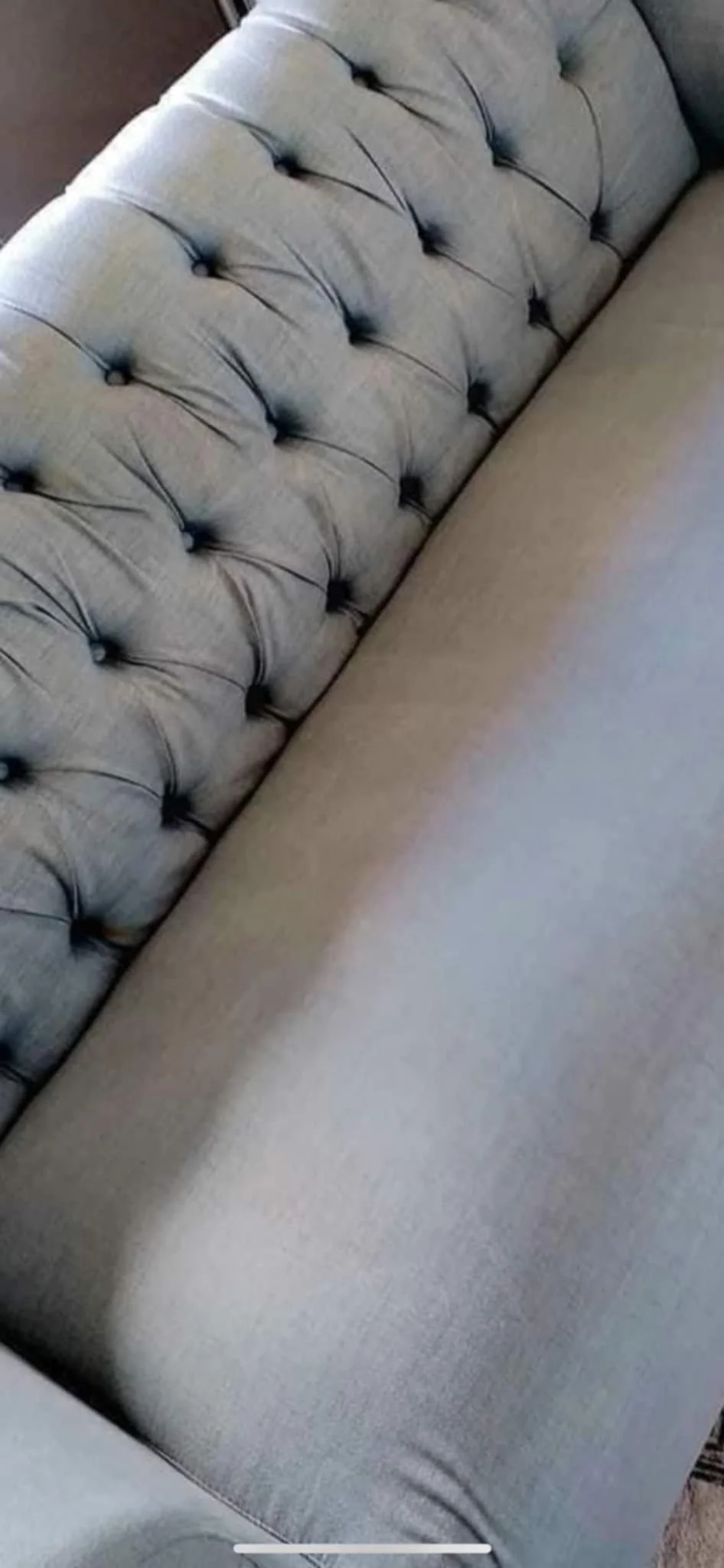 Close-up of a gray upholstered tufted sofa with button-tufted backrest.