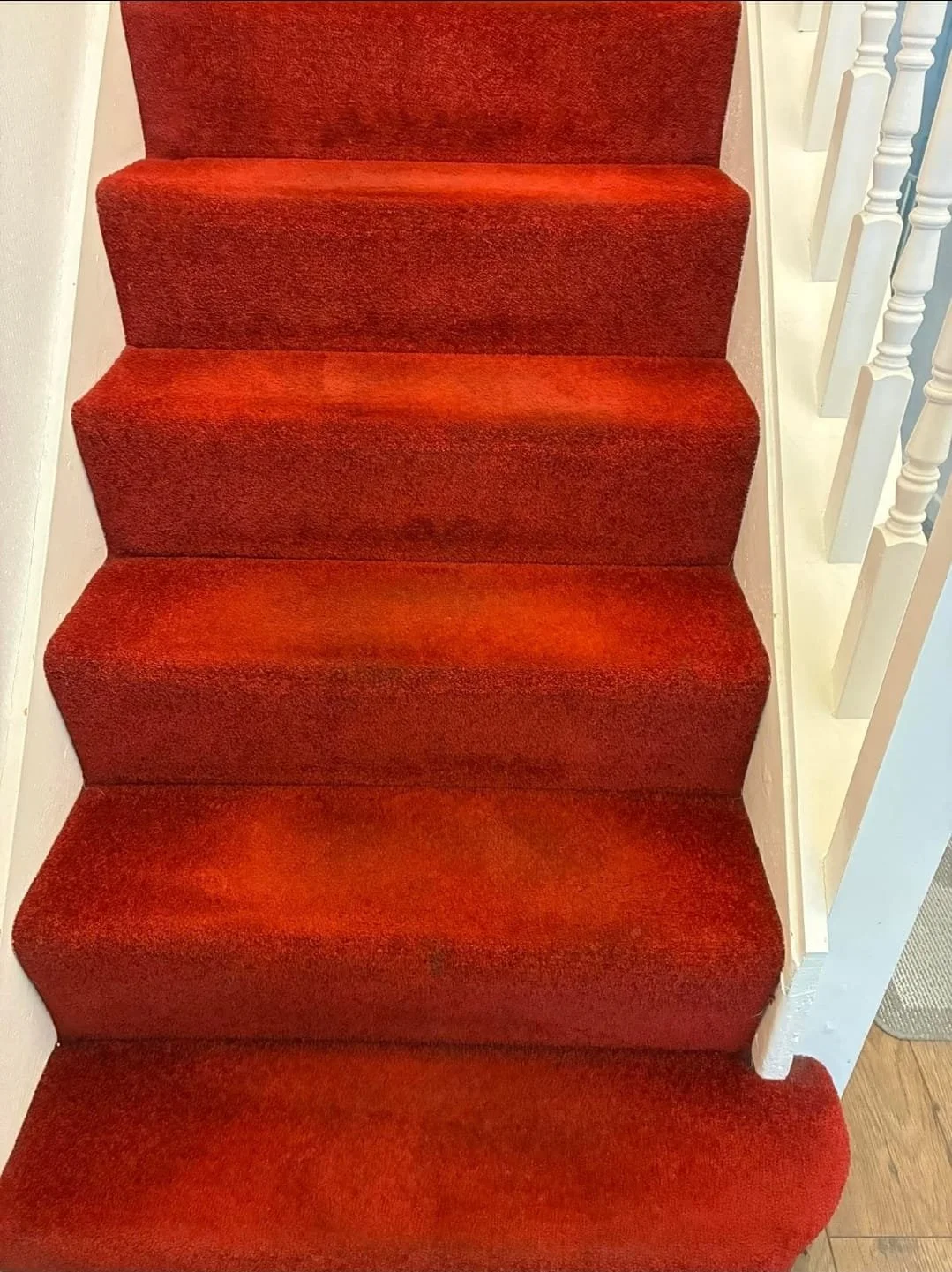 Top view of a red-carpeted staircase with white walls and a white spindled railing on the right side.