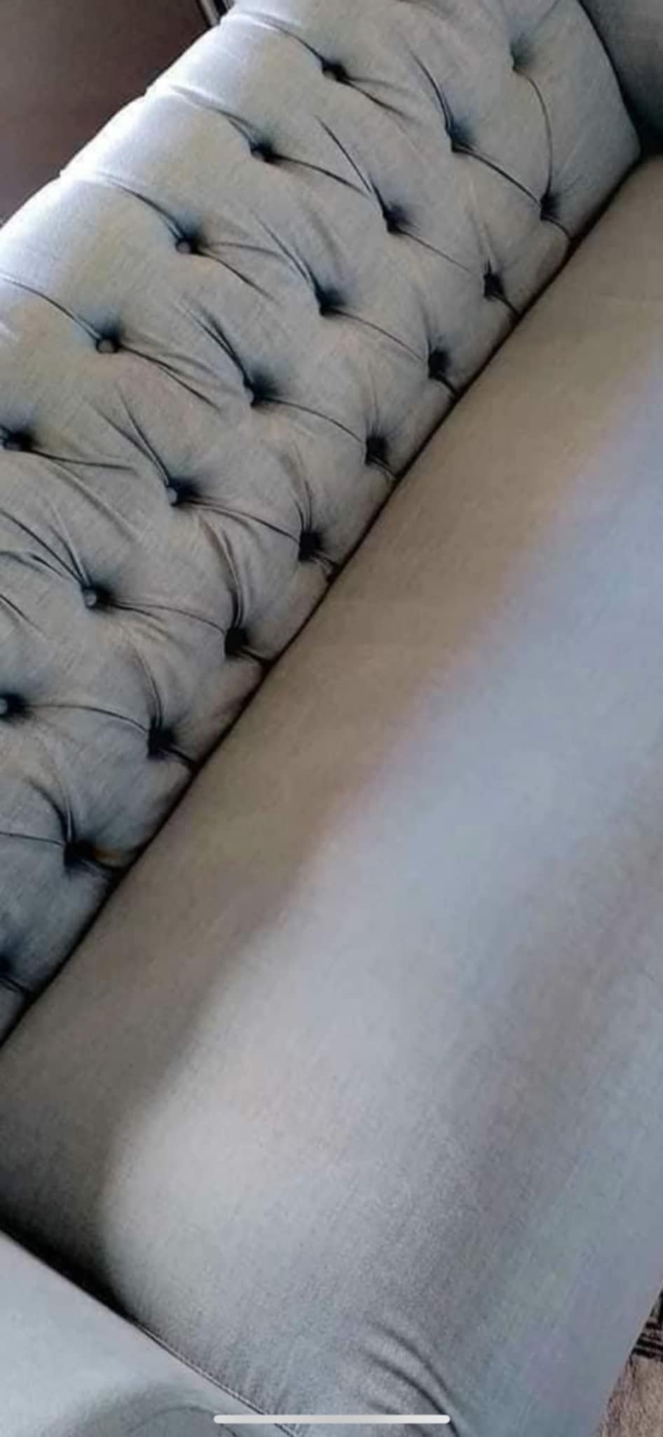 A gray tufted sofa with button accents, positioned next to a plain beige or light gray cushion or section.