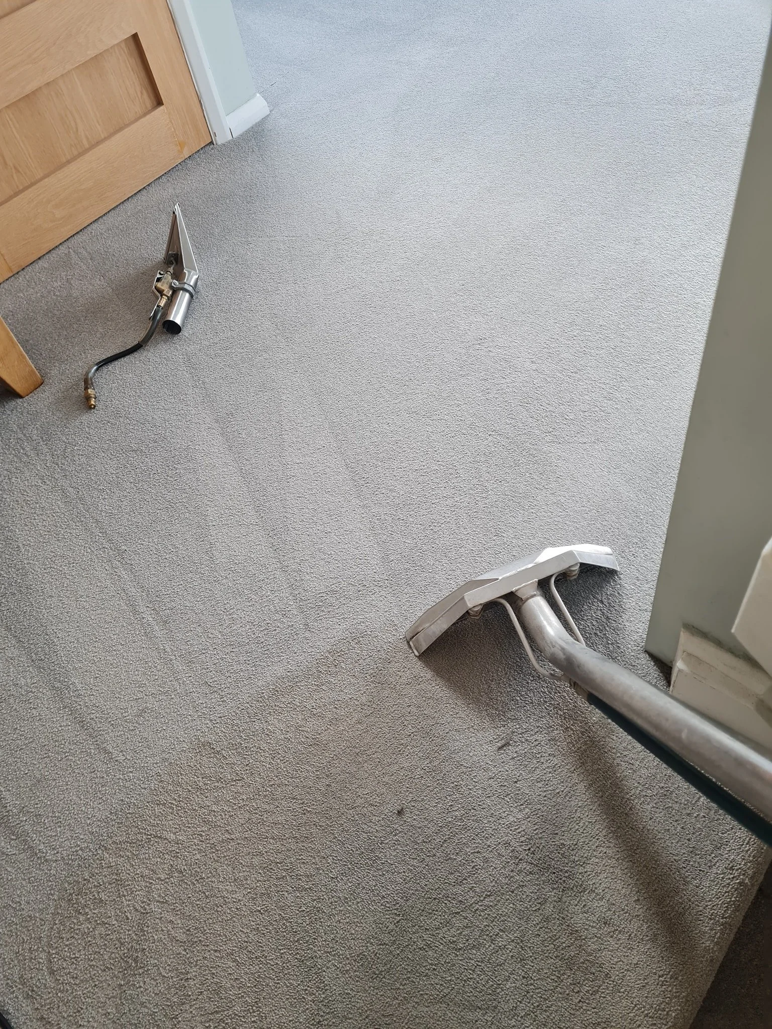 Carpet cleaner wand on the carpeted floor next to a disassembled vacuum attachment.