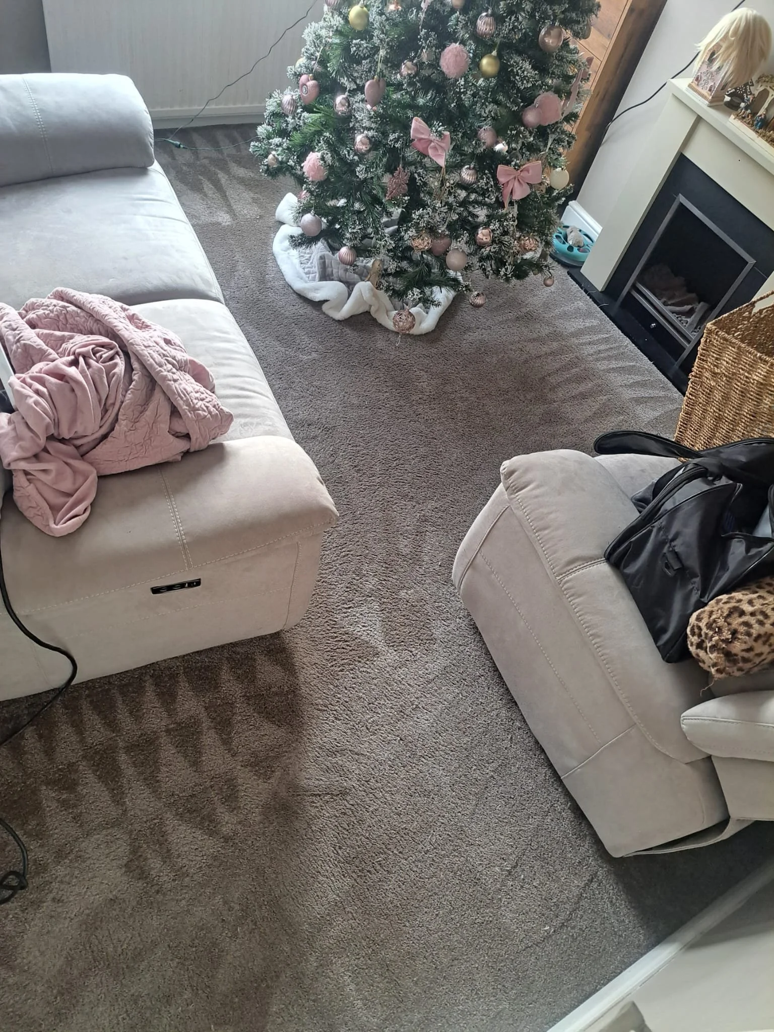 Living room with decorated Christmas tree, beige couches, a fireplace, a leopard-print pillow, a black bag, and pink and white blanket.