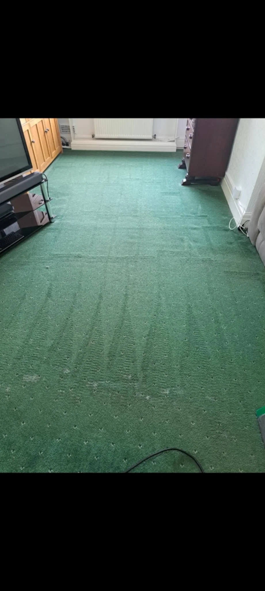 Green carpeted floor in a living room with furniture and a radiator in the background.