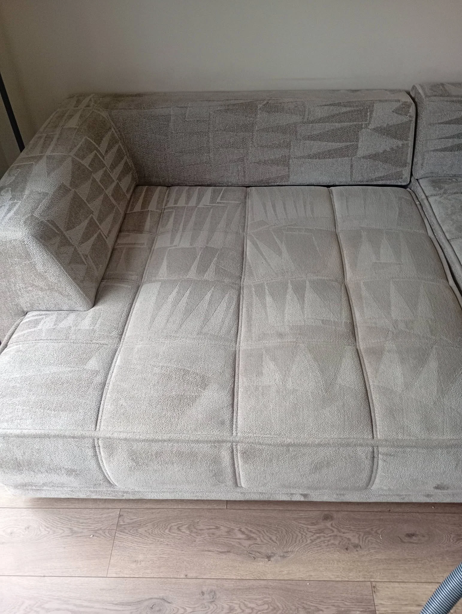 A light-colored, patterned fabric sofa with a wooden floor underneath.