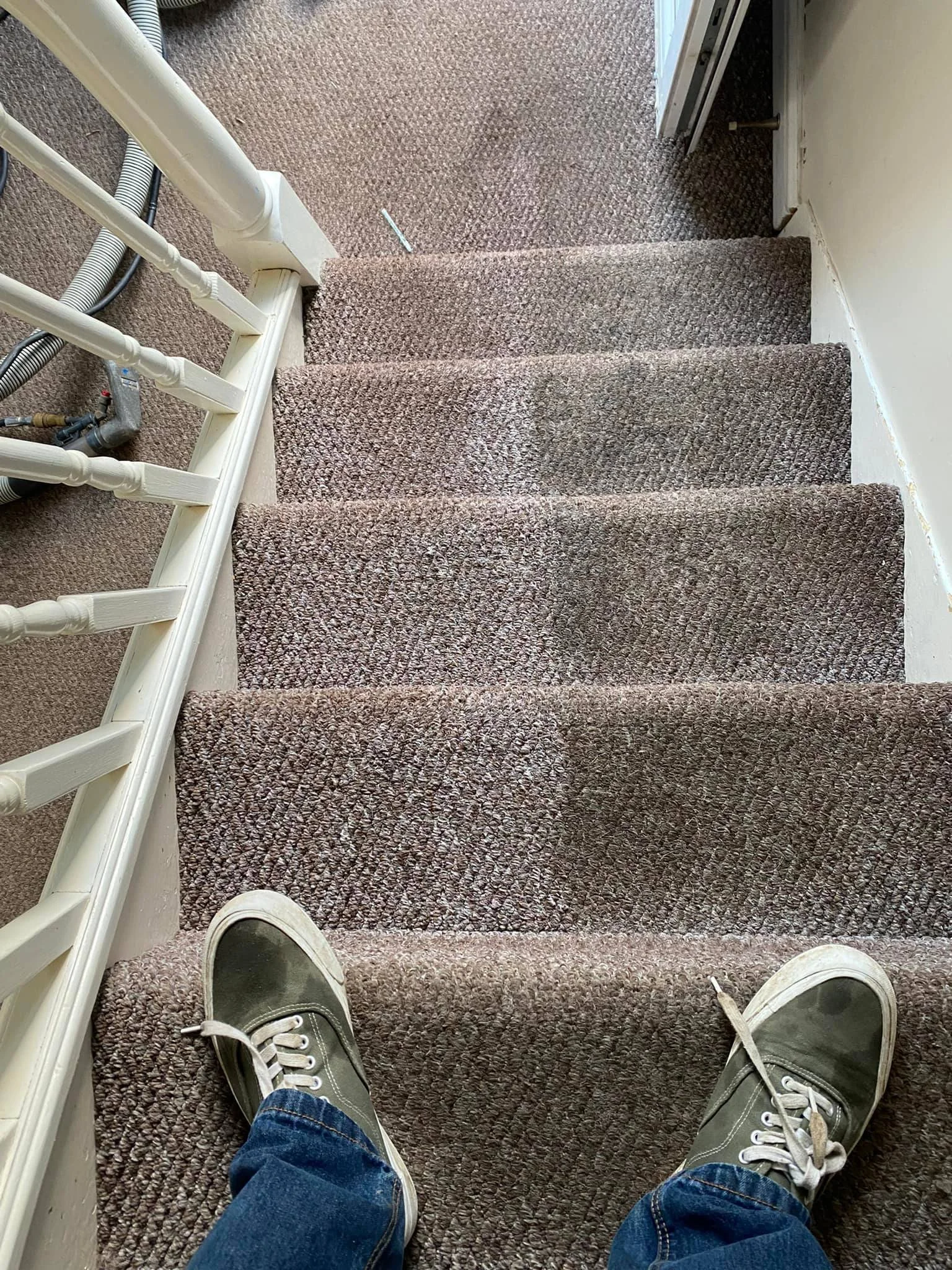 Person standing on carpeted stairs, wearing green sneakers and jeans, with visible shoes and part of the staircase railing.