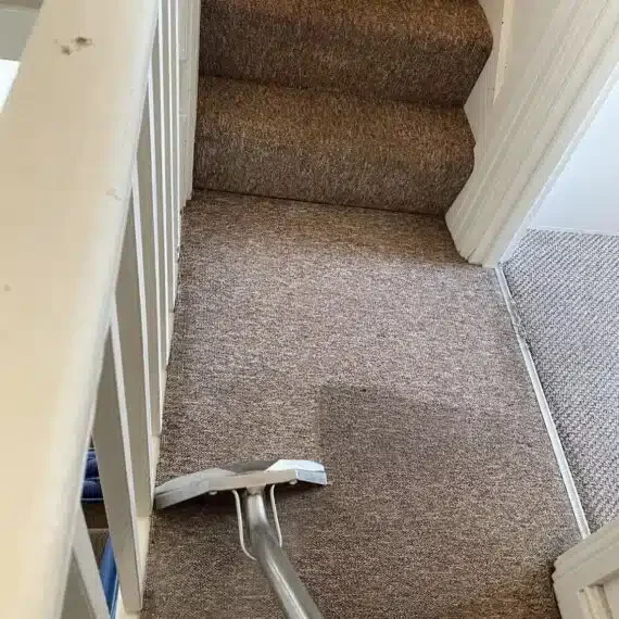 A vacuum cleaner being used to clean a carpeted staircase and landing.