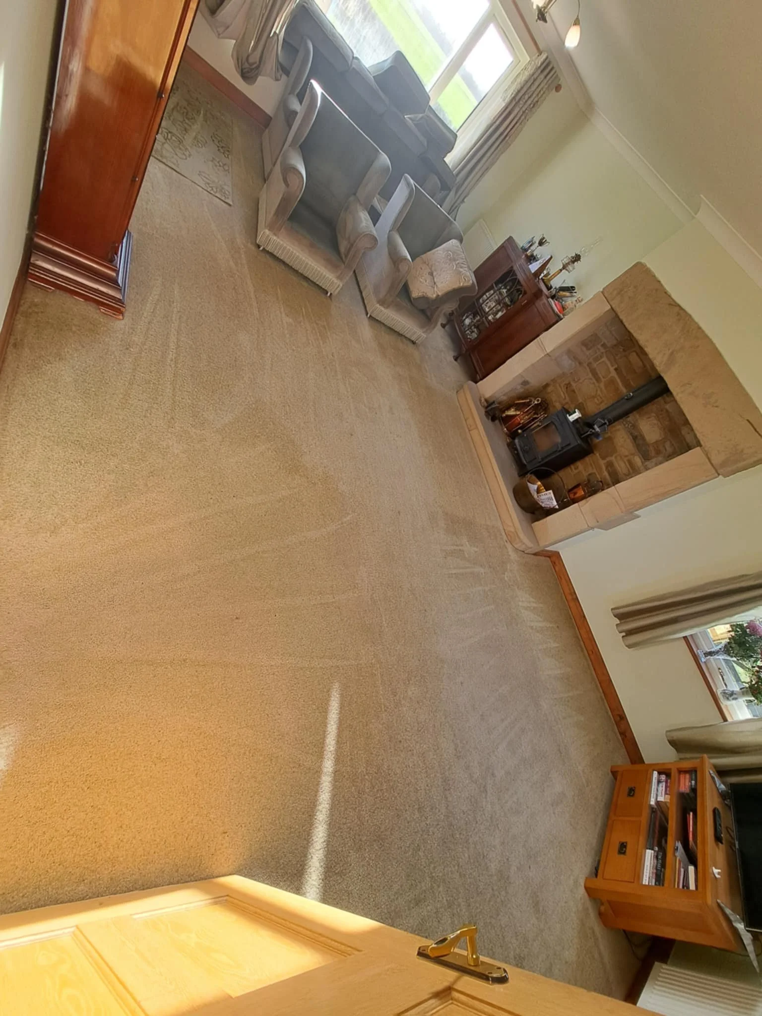Living room with beige carpet, a window with curtains, a fireplace with a chimney, a small wooden bookcase, and three beige armchairs near the window.