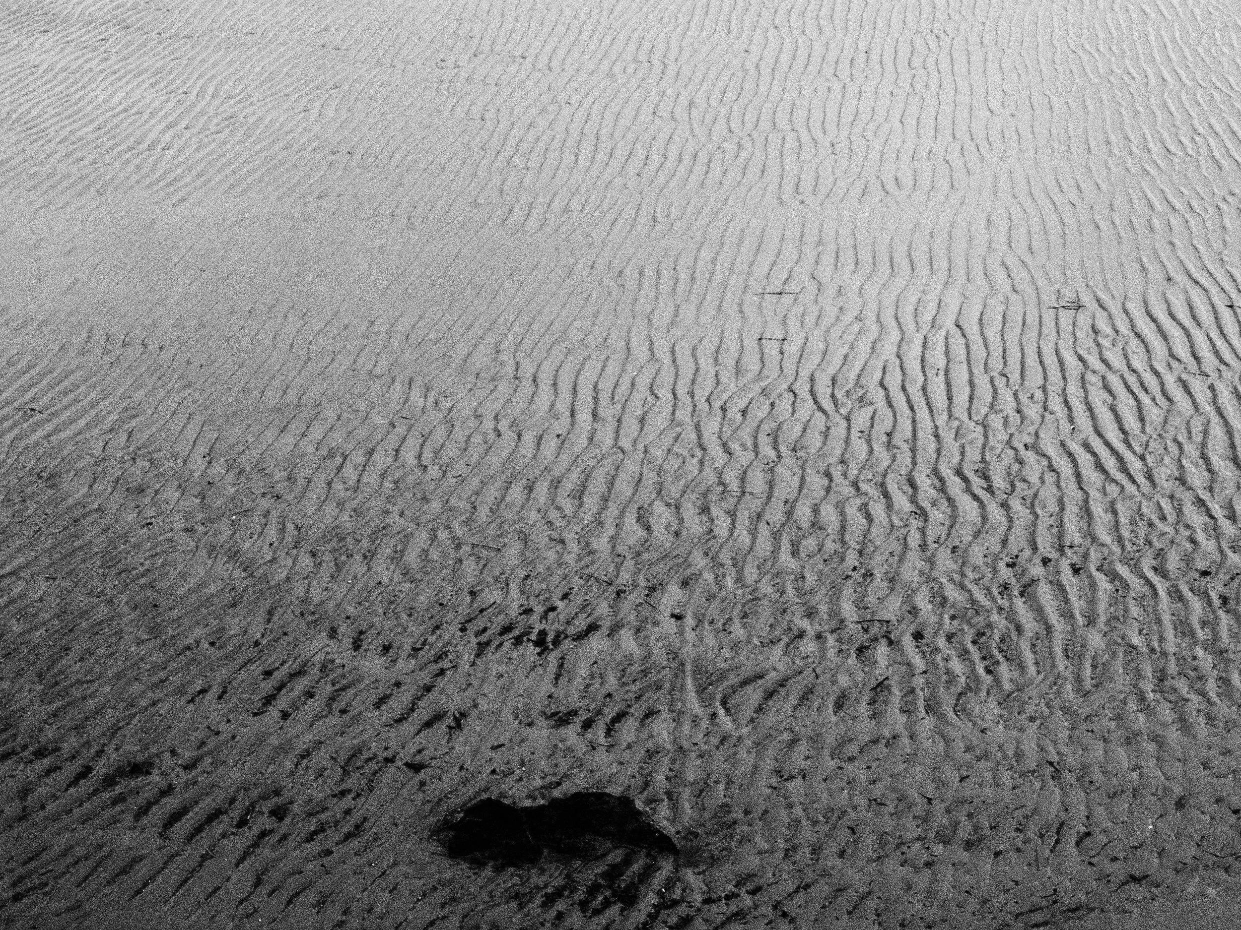 Close-up of sand with ripples and a solitary hole in the foreground.