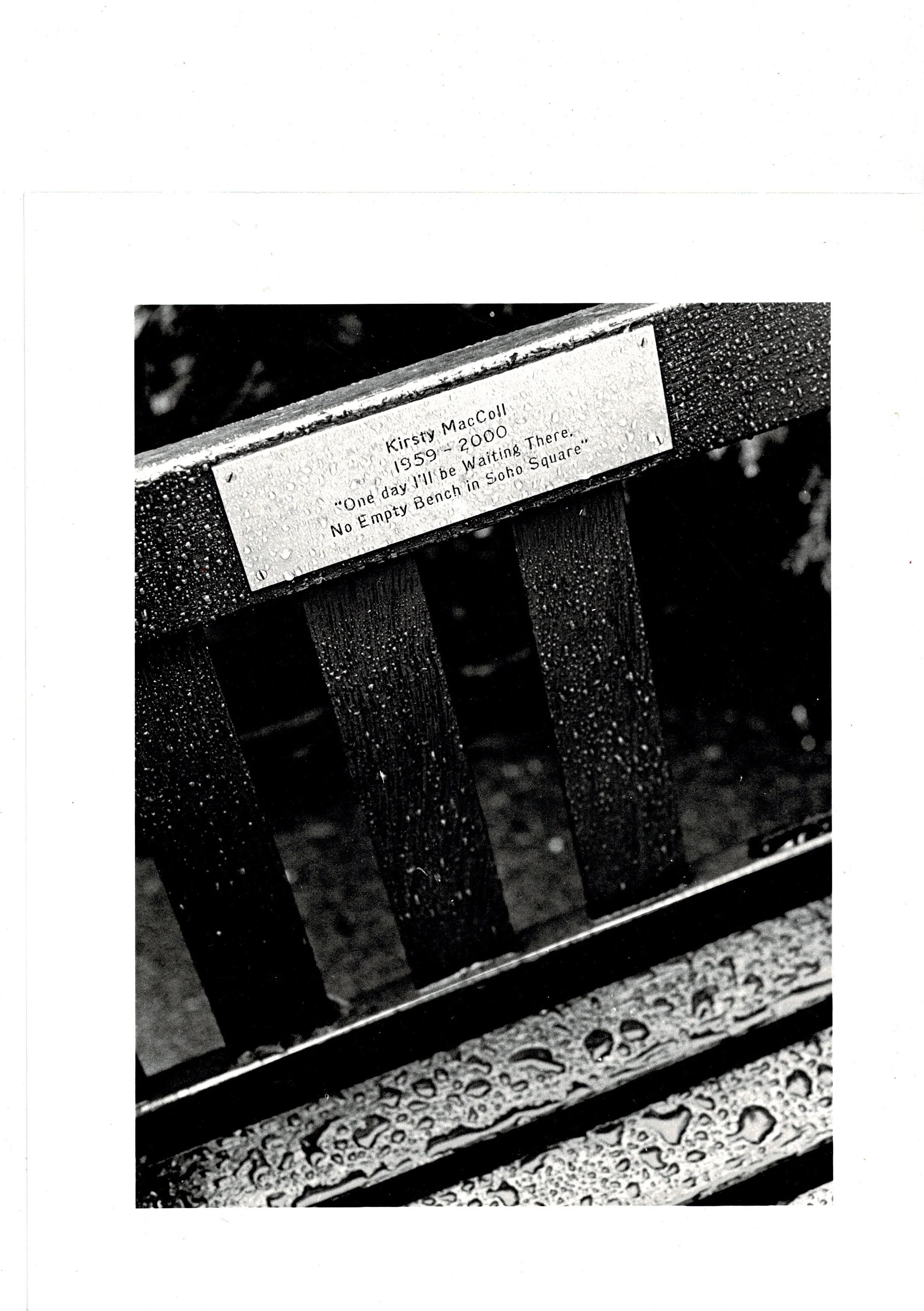 Black and white photograph of the rain-spotted Kirsty MacColl memorial bench in Soho Square, hand-printed darkroom analogue print