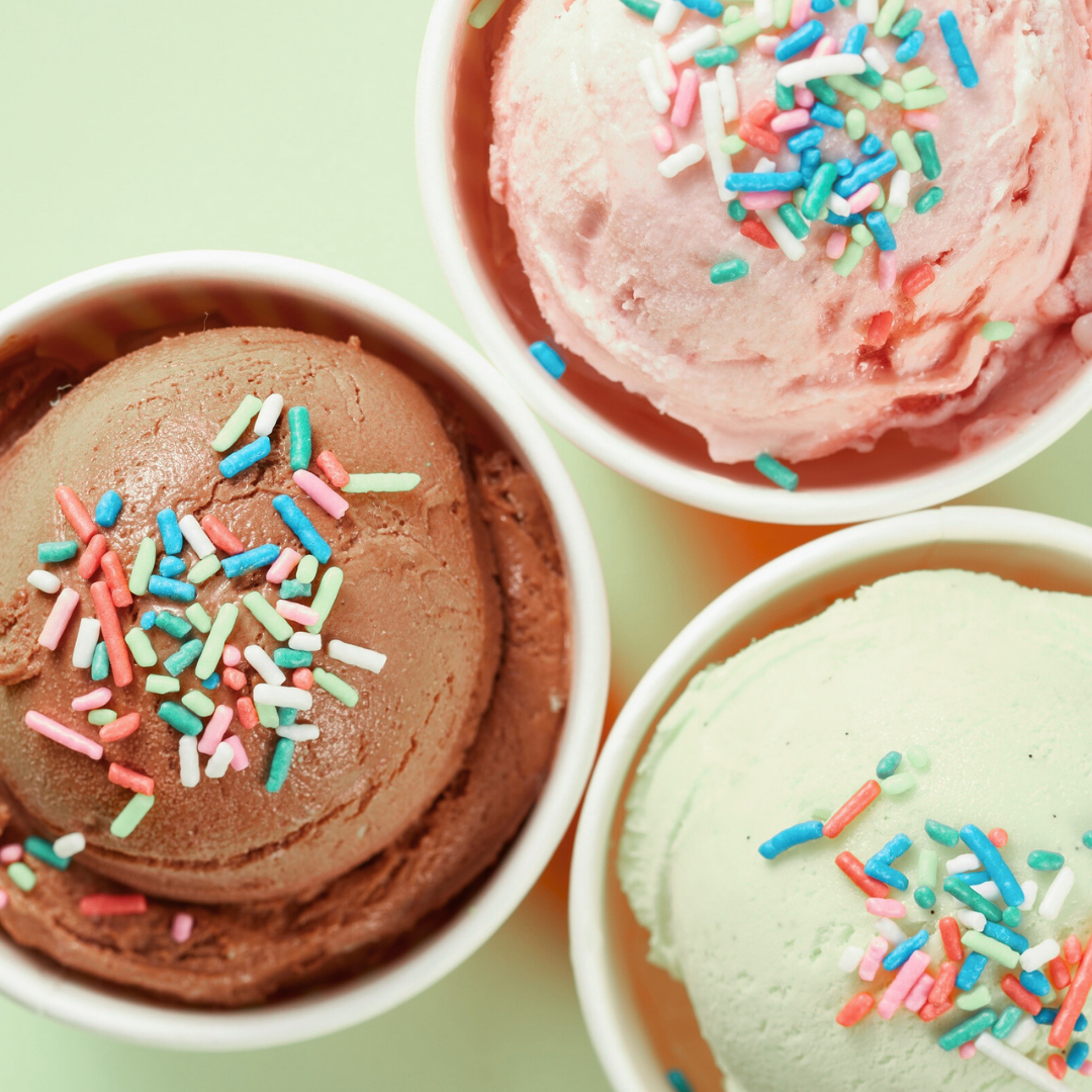 Trois coupes de glace à la confiserie, avec des copeaux de sucre colorés, dans des contenants en plastique blanc.