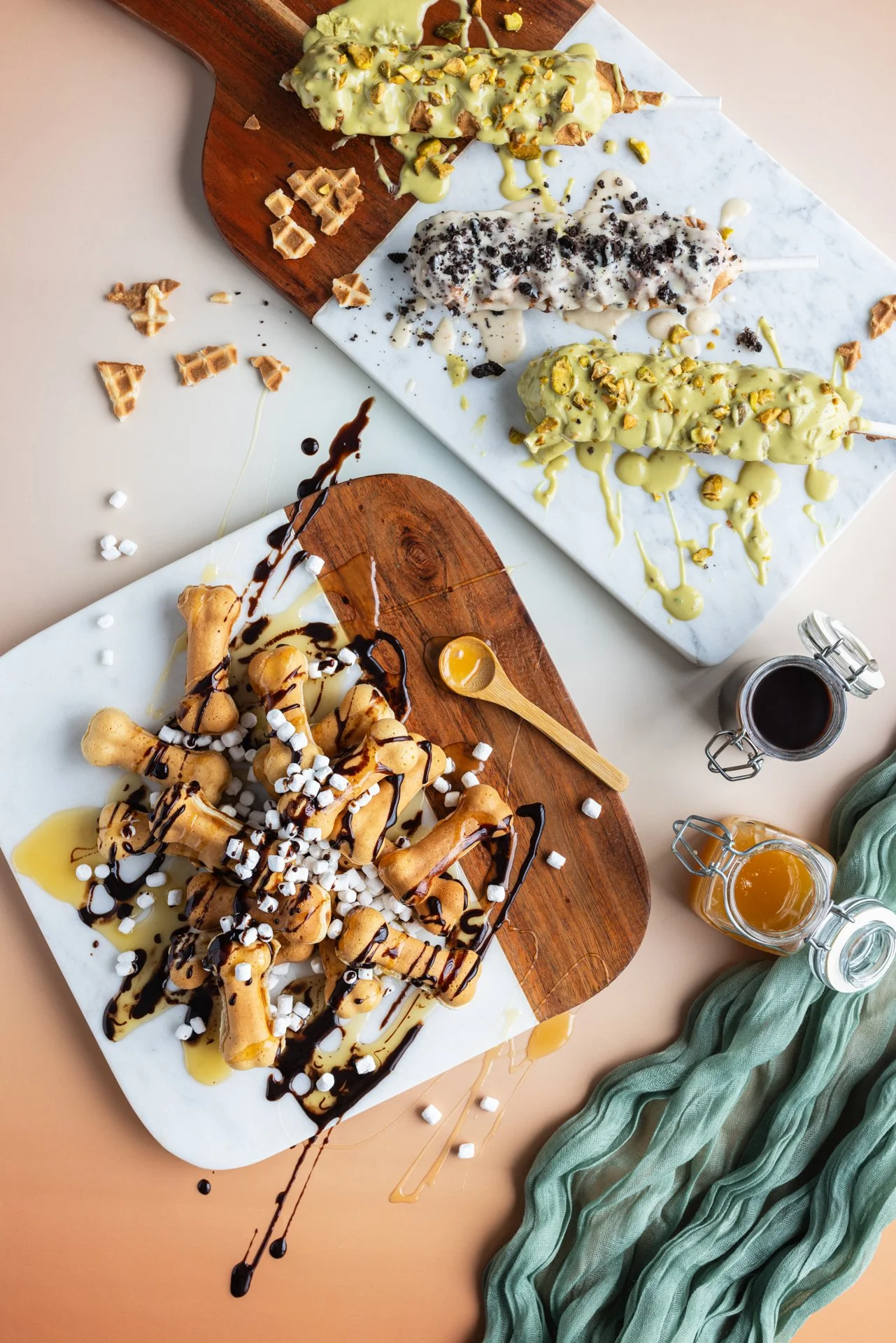 Assortiment de nourriture, comprenant des glaces en bâton, des biscuits, du sirop, et une sauce au chocolat, présentés sur des planches en bois et des surfaces en marbre.