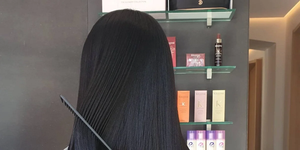 Back of a person with long, straight, shiny reddish-brown hair in a salon setting.