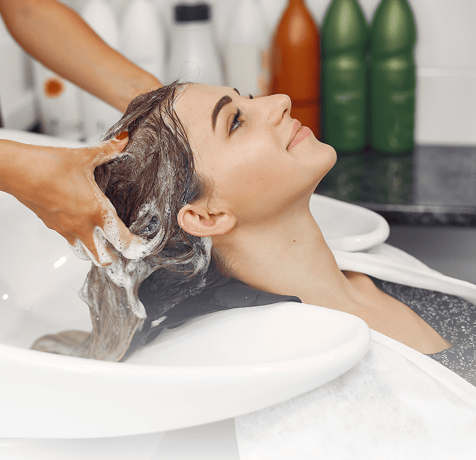 Woman getting her hair washed at a salon sink, smiling and relaxing with her eyes closed.
