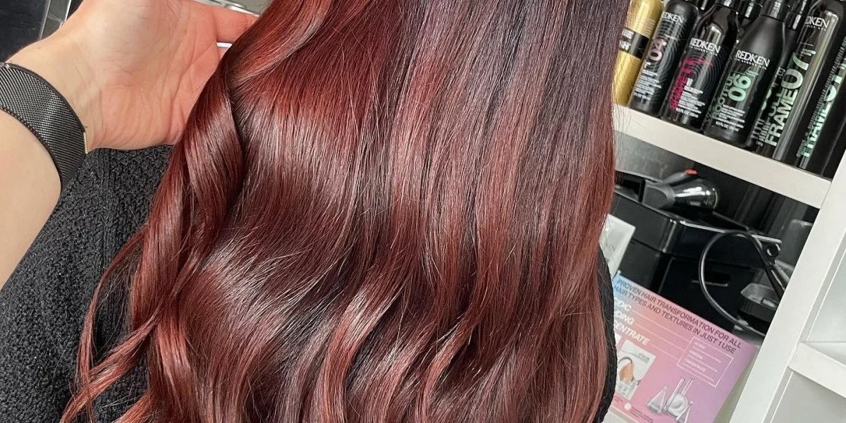 Close-up of a person’s head with wavy, reddish-brown shiny hair, touching the hair at the crown.