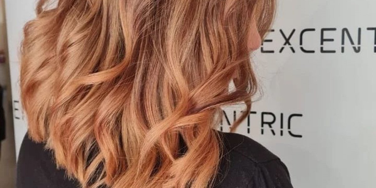 A woman with shoulder-length, curly, peach-blonde hair standing in front of a white wall with black text.