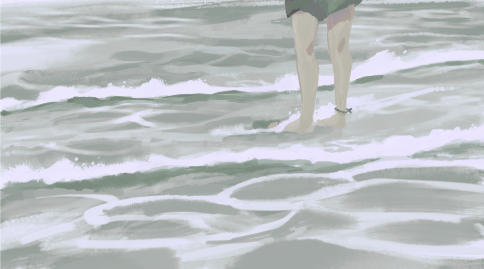 Person standing in the ocean water with waves, wearing black shorts and an ankle bracelet.