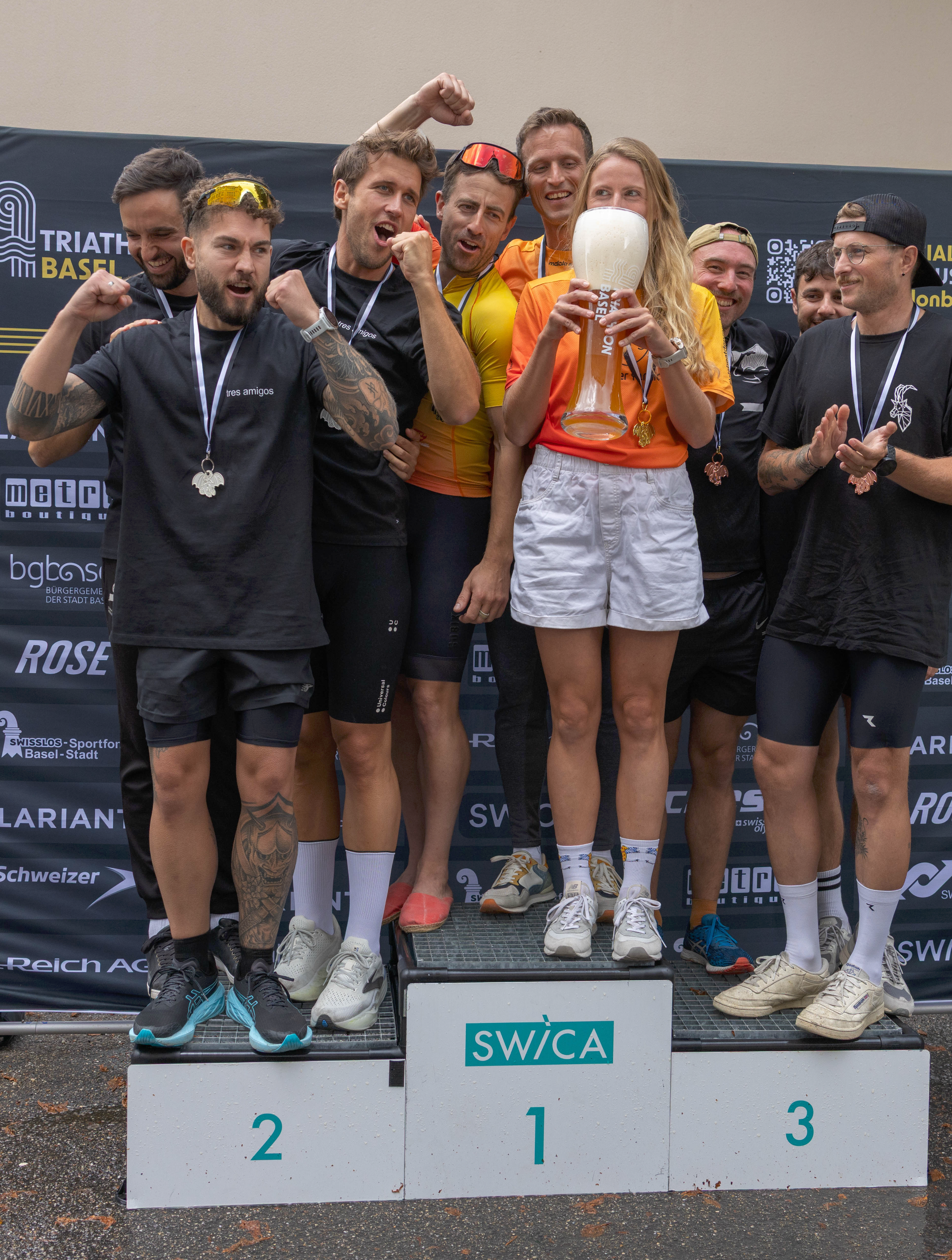 Gruppe von Triathleten auf dem Siegerpodest, die feiern und eine Trophäe halten bei einem Triathlon-Event in Basel.