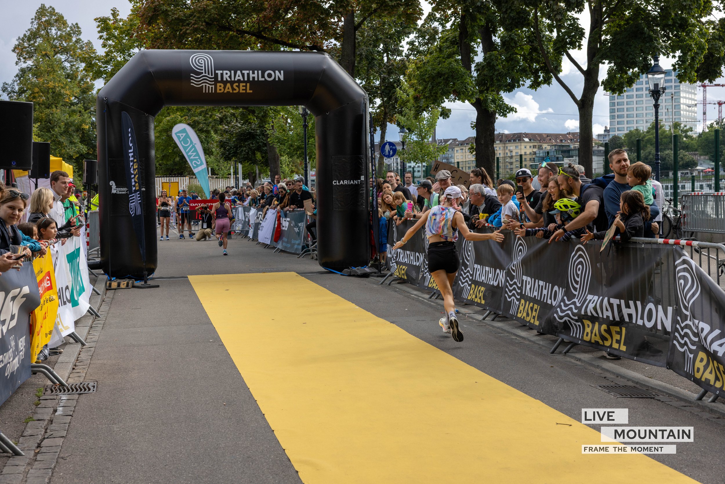 Ein weiblicher Läufer läuft an der Ziellinie beim Triathlon in Basel, während eine Menschenmenge die Zuschauer entlang der Strecke anfeuert.
