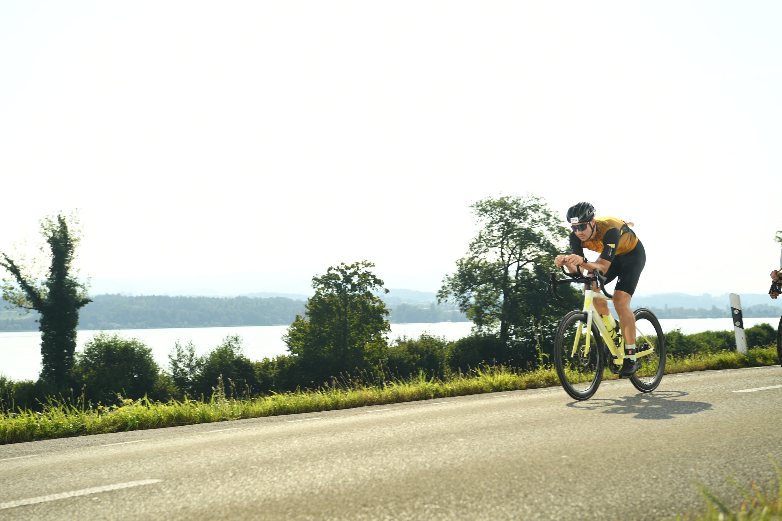 Ein Fahrradfahrer in sportlicher Kleidung und Helm, der auf einer Landstraße in der Nähe eines Sees unterwegs ist.