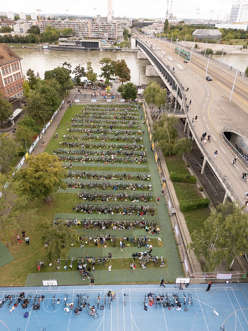Ein Fußballfeld mit Fahrrädern und Menschen, daneben eine Brücke über einem Fluss in einer Stadt.