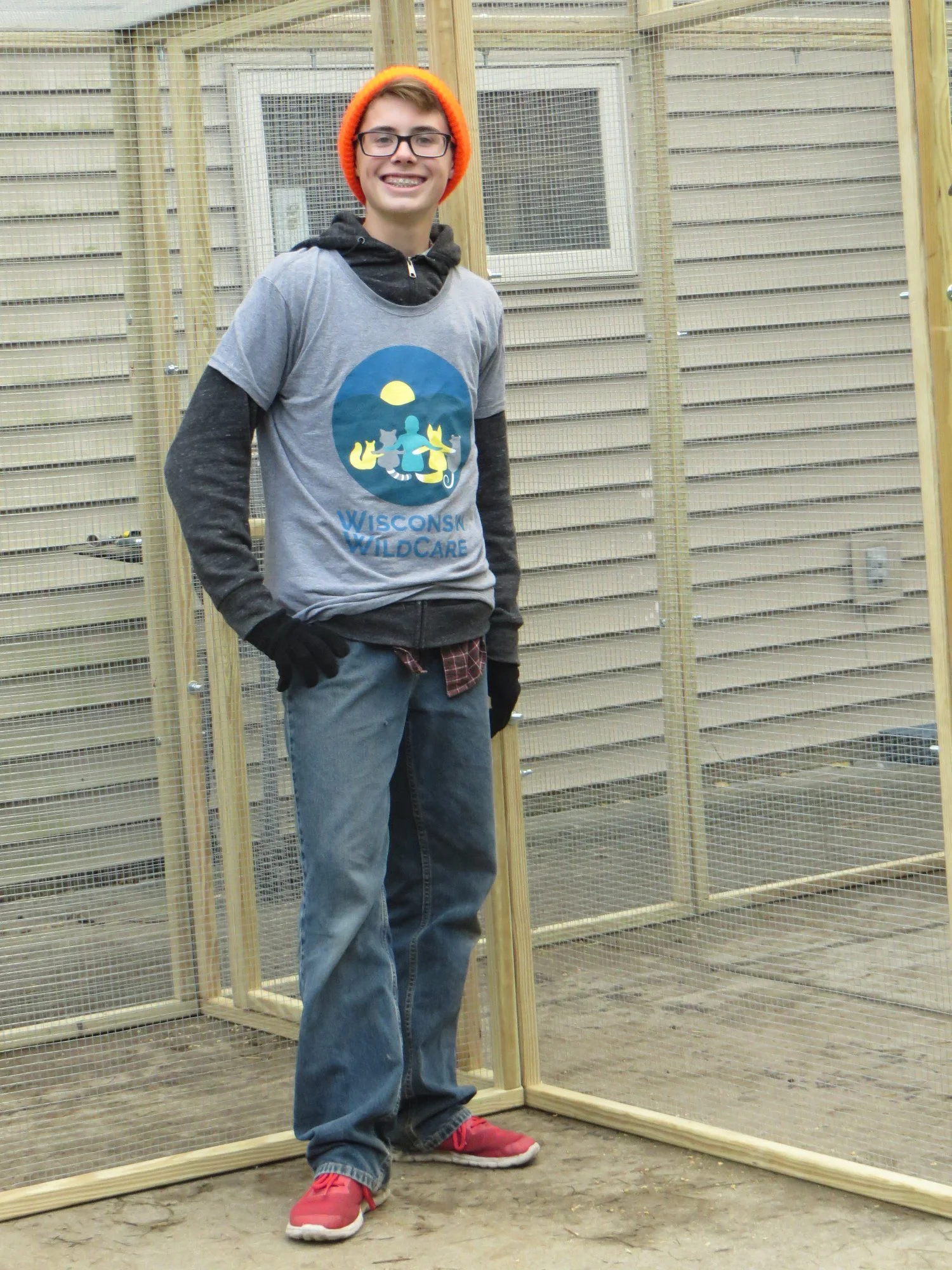 Person in a Wisconsin WildCare T-shirt and orange winter cap smiling near squirrel enclosure