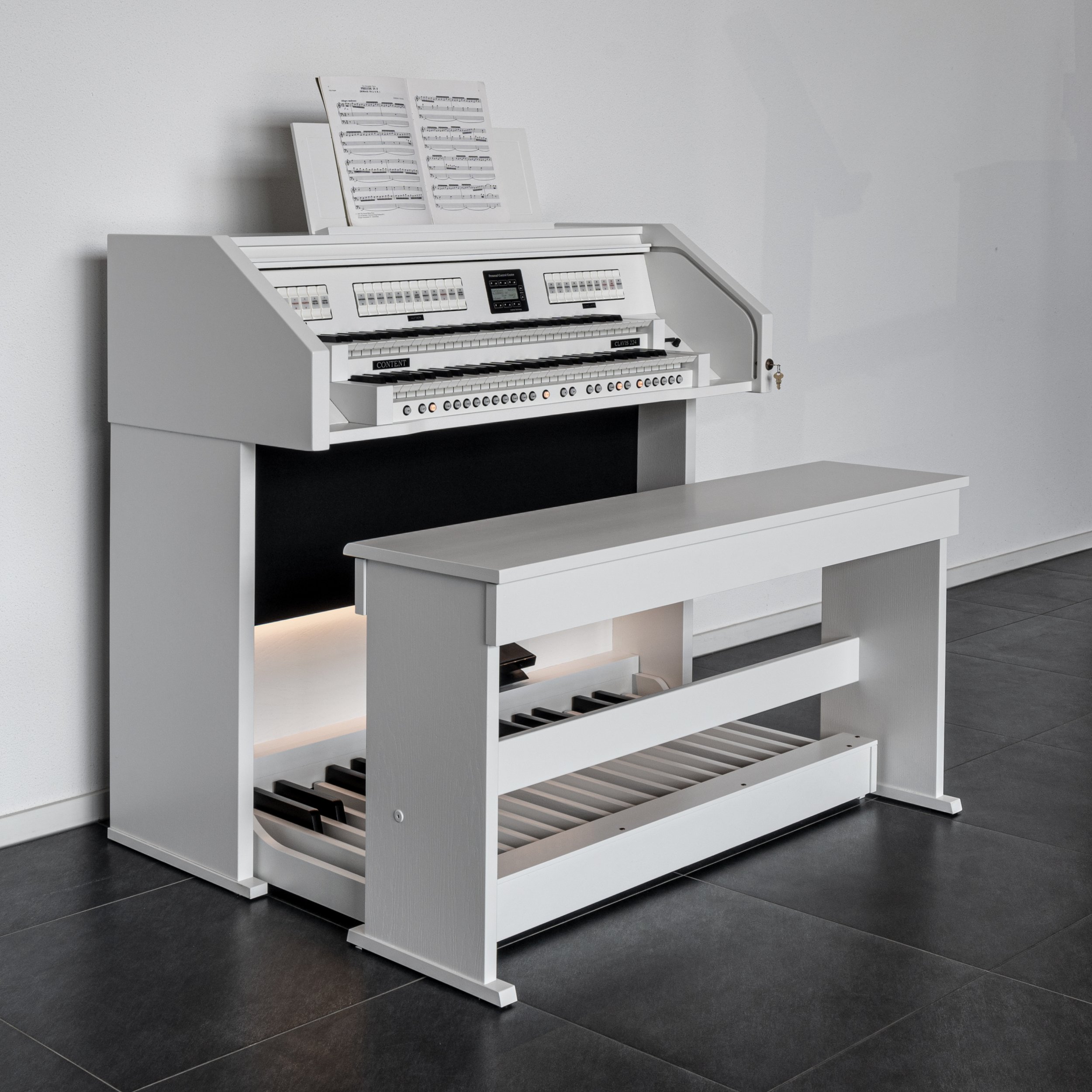 White digital organ with sheet music on display and a matching bench in a room with white walls and dark tiled floor.