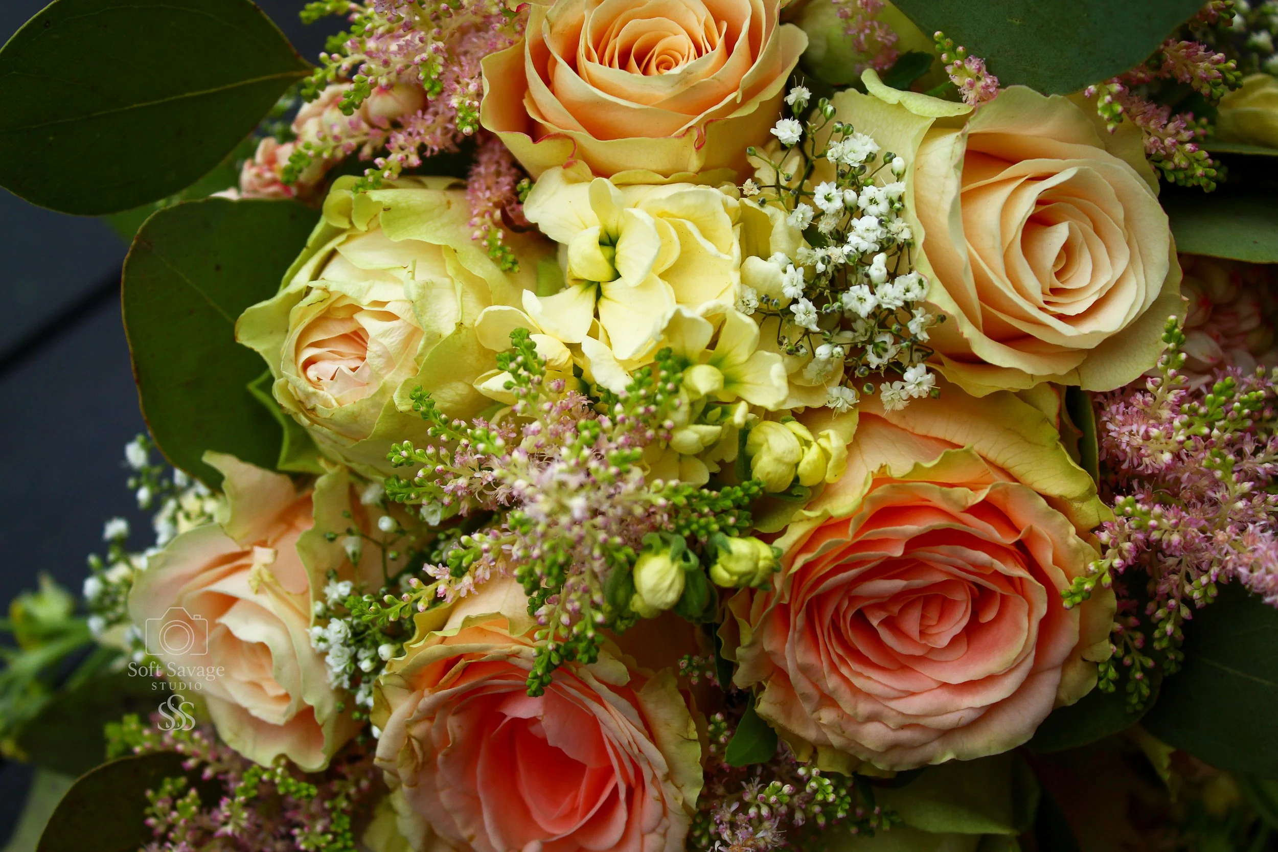 Ein Blumenstrauß mit gelben, rosafarbenen und weißen Rosen, kleinen weißen Blümchen und grünen Blättern.