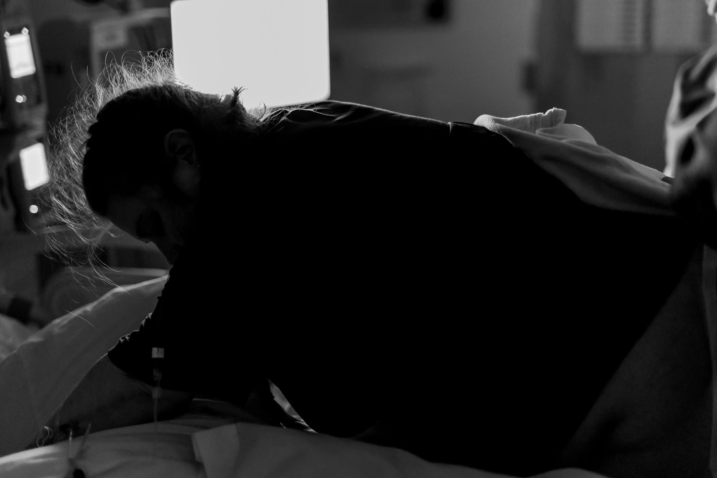 A person on their hands and knees in a hospital bed in labor, in a dimly lit room. 