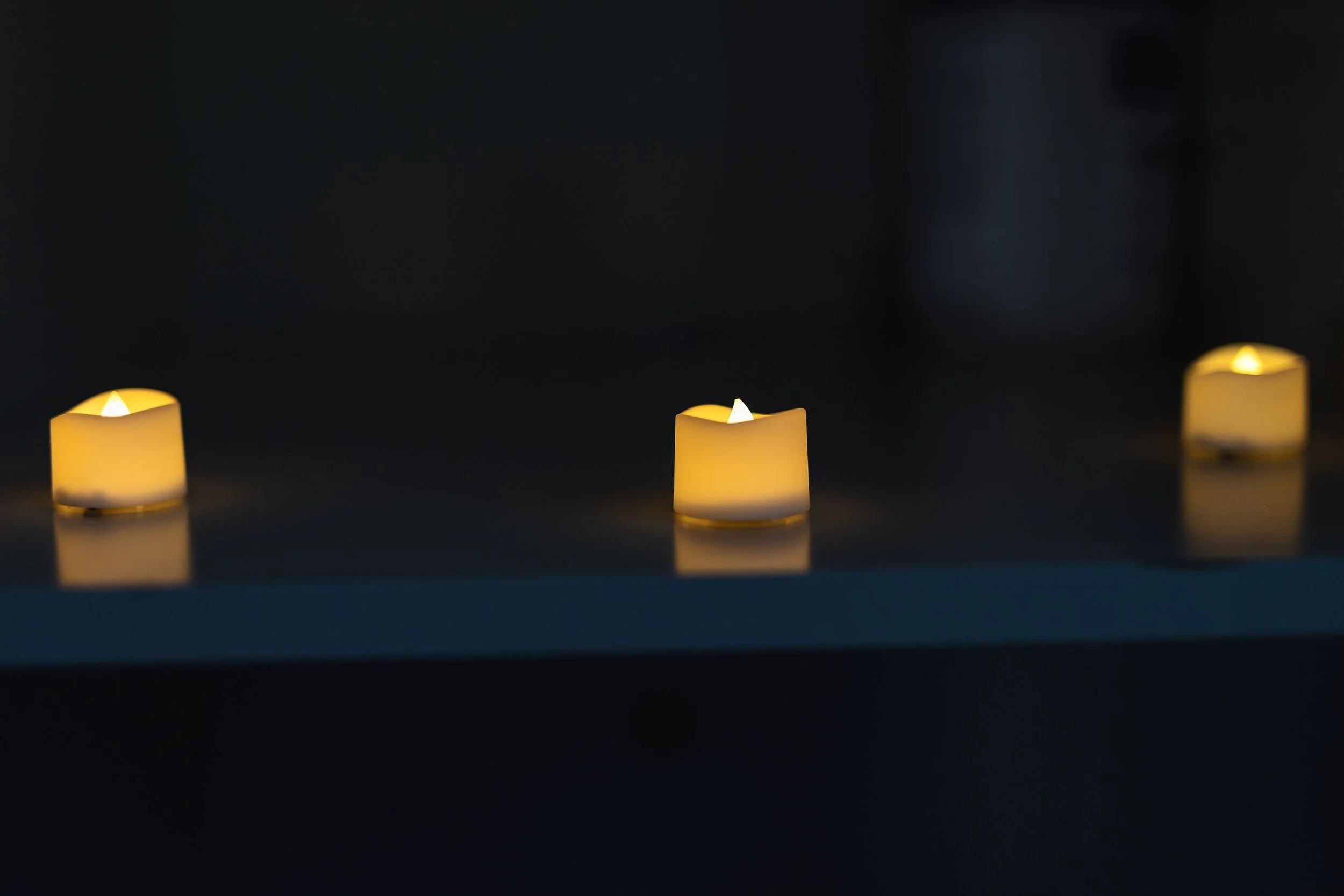 Three flickering yellow candles on a dark surface in a dimly lit setting.