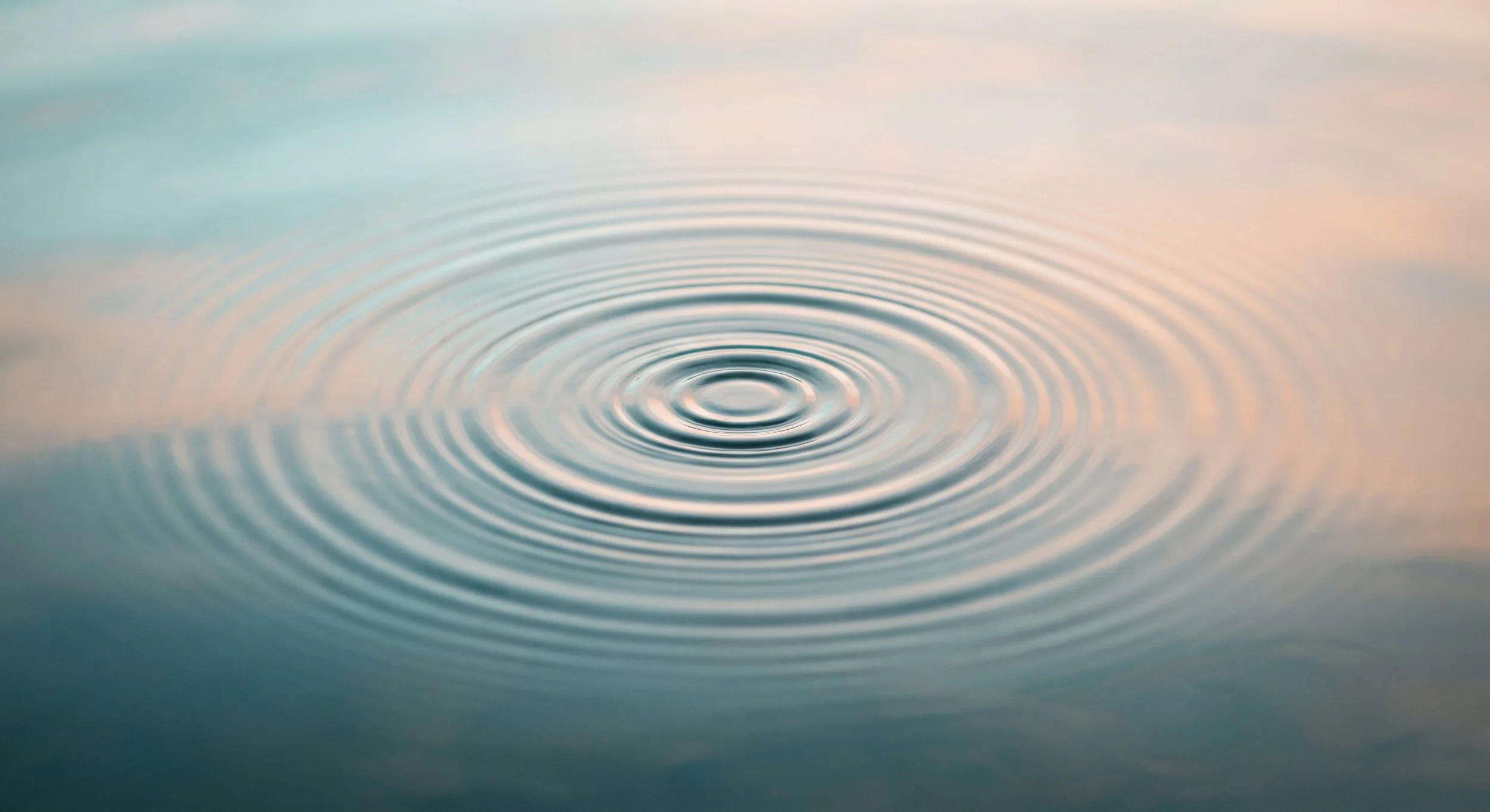 Vagues concentriques formant des cercles sur une surface d'eau calme, avec un fond pastel flou.