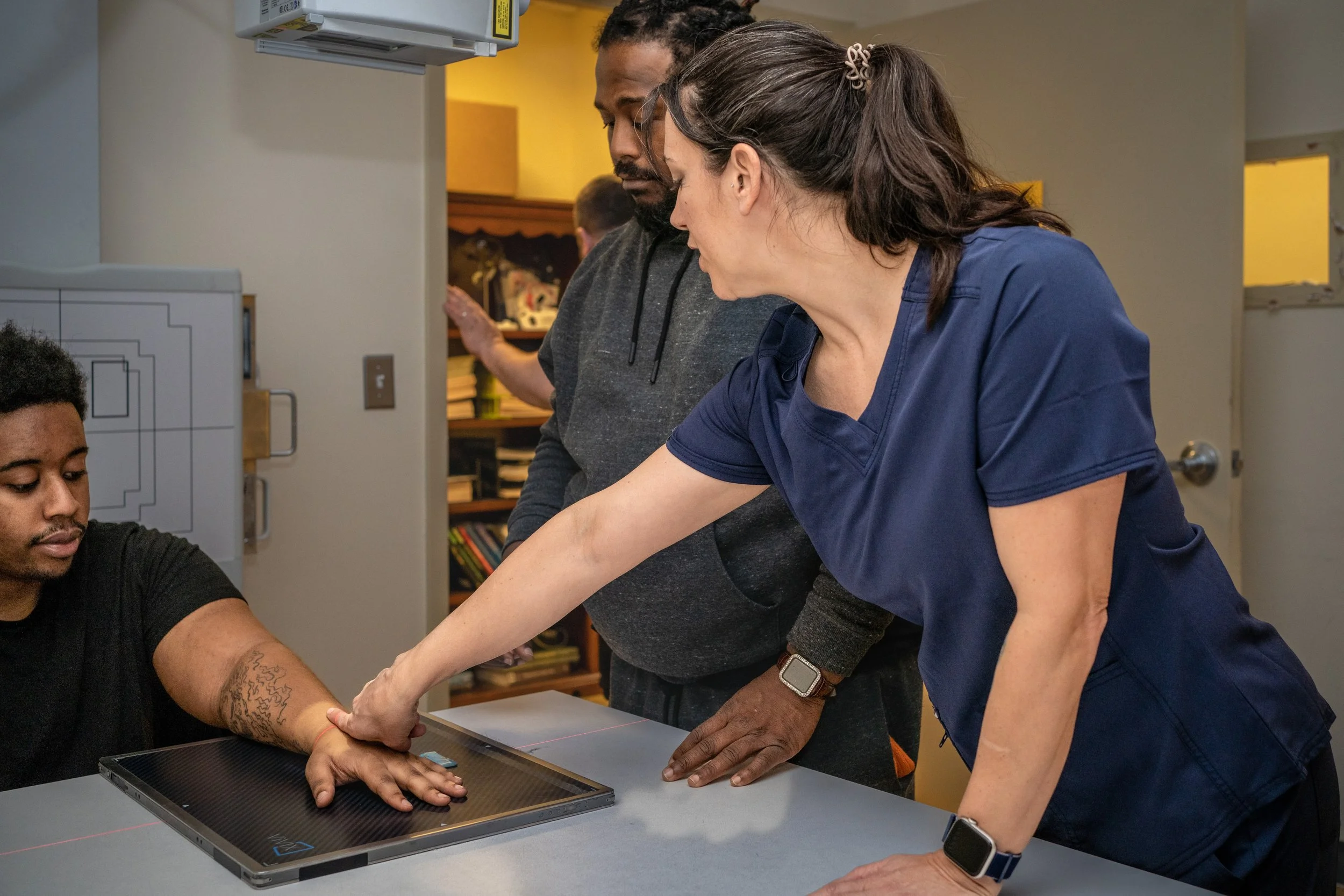 An instructor points to the area on another person's arm for a technician in training