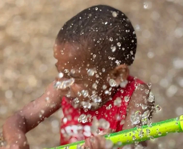 A child holding a squirting tube seen through water droplets