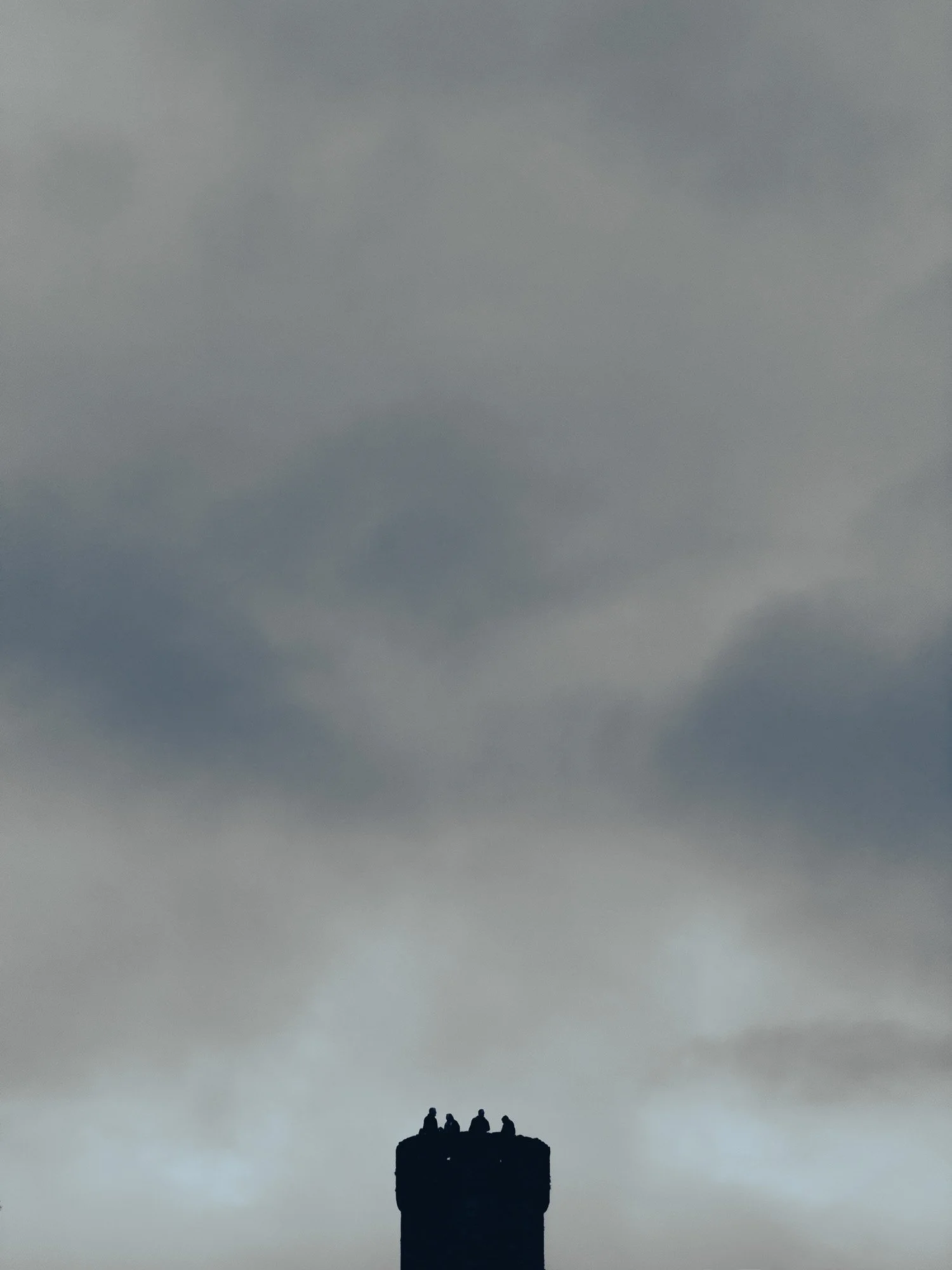 Silhouette of four people sitting on top of a chimney with cloudy sky in the background.