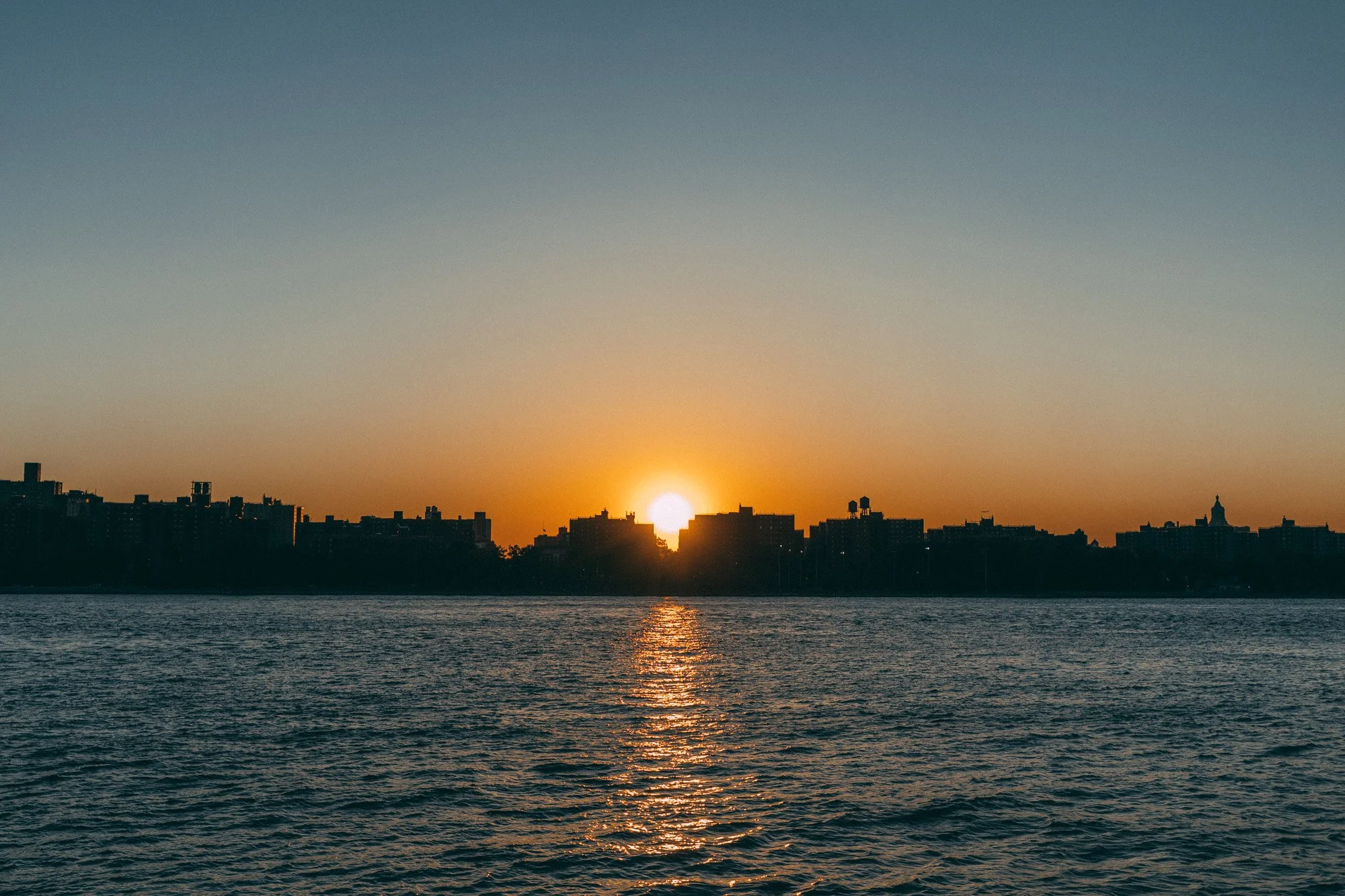 Sun setting behind a city skyline across a body of water.