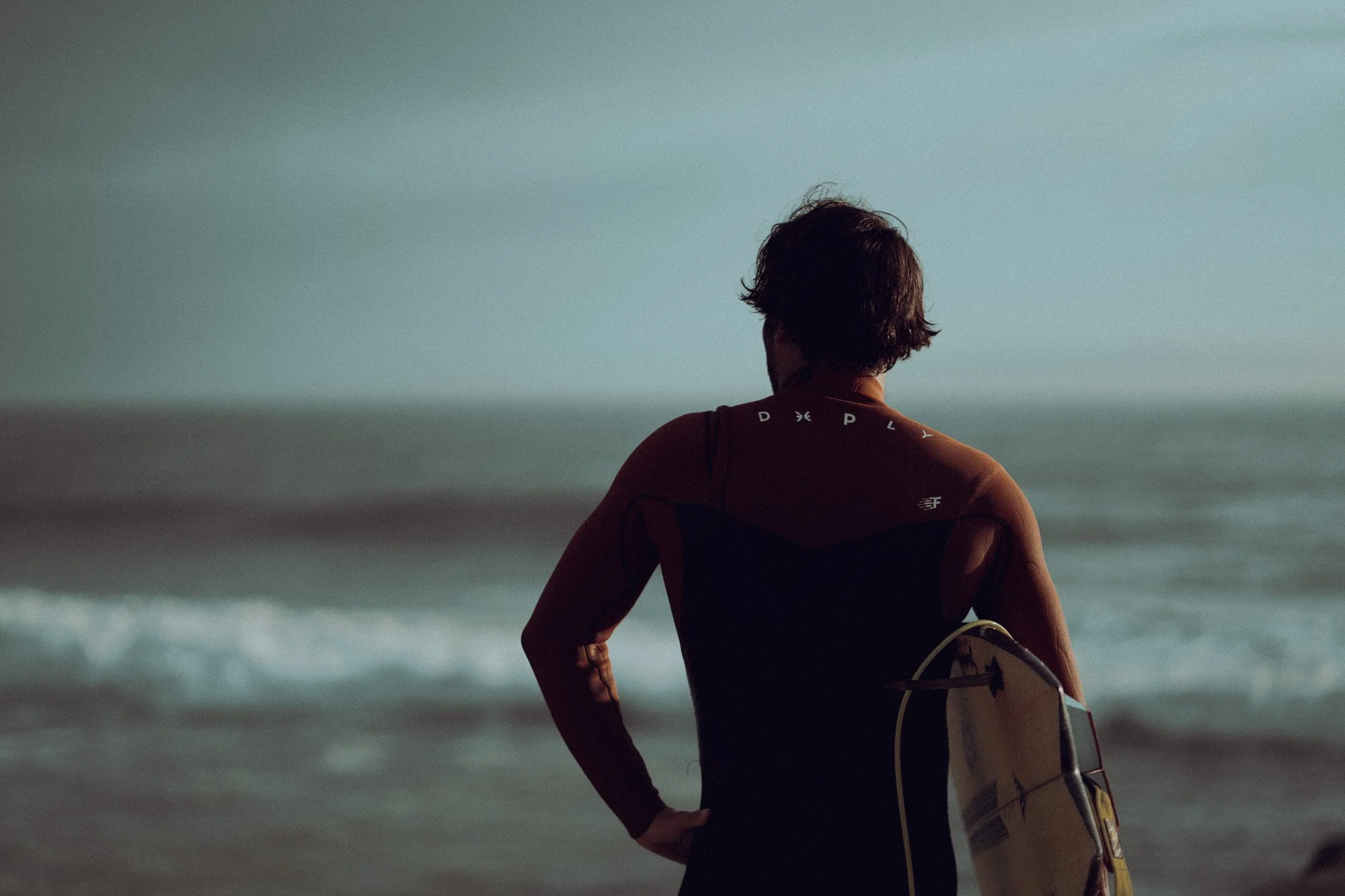 Man holding surfboard standing on the beach facing the ocean
