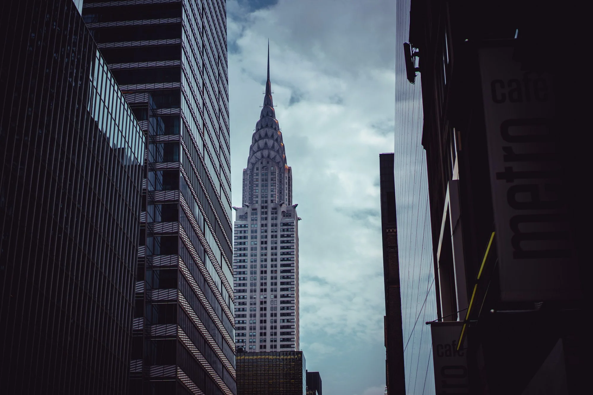 View of the Chrysler Building framed by surrounding skyscrapers on a cloudy day in New York City.