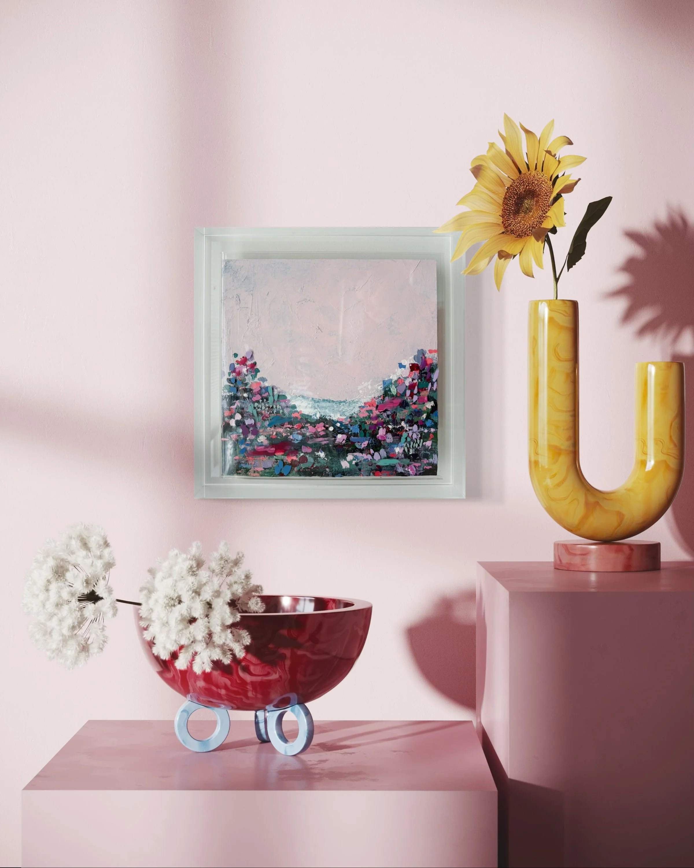 A pink wall decorated with a framed landscape painting, a yellow marble vase with a sunflower, a pink pedestal, a red bowl with white flowers, and part of a pink table.