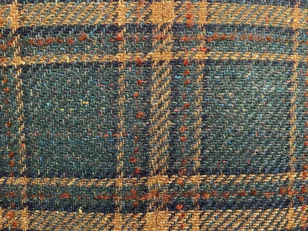 Close-up of a woven fabric tweed with a plaid pattern in shades of brown, navy blue, and red.