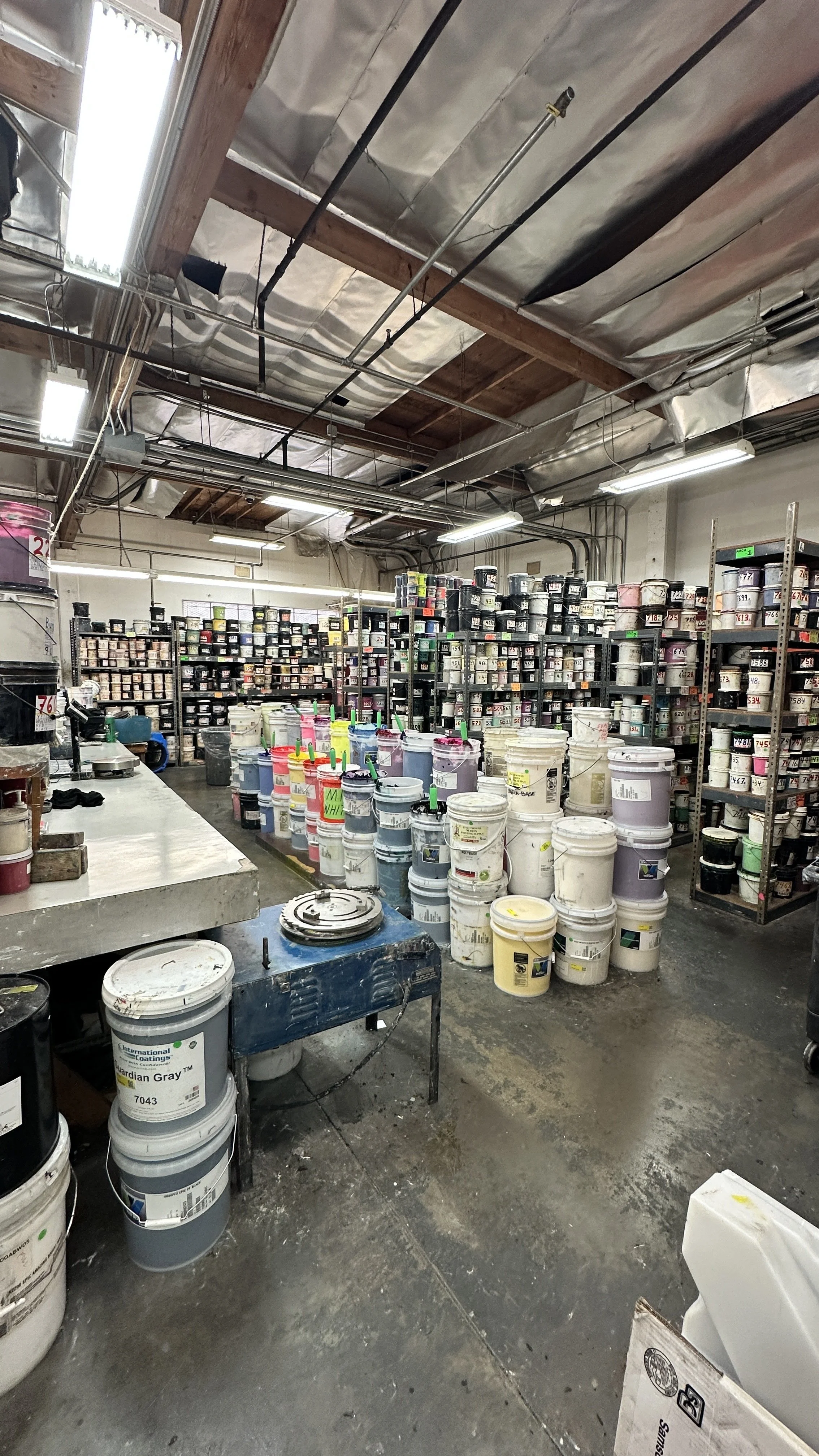 A store filled with shelves and buckets of paint in various colors and sizes.