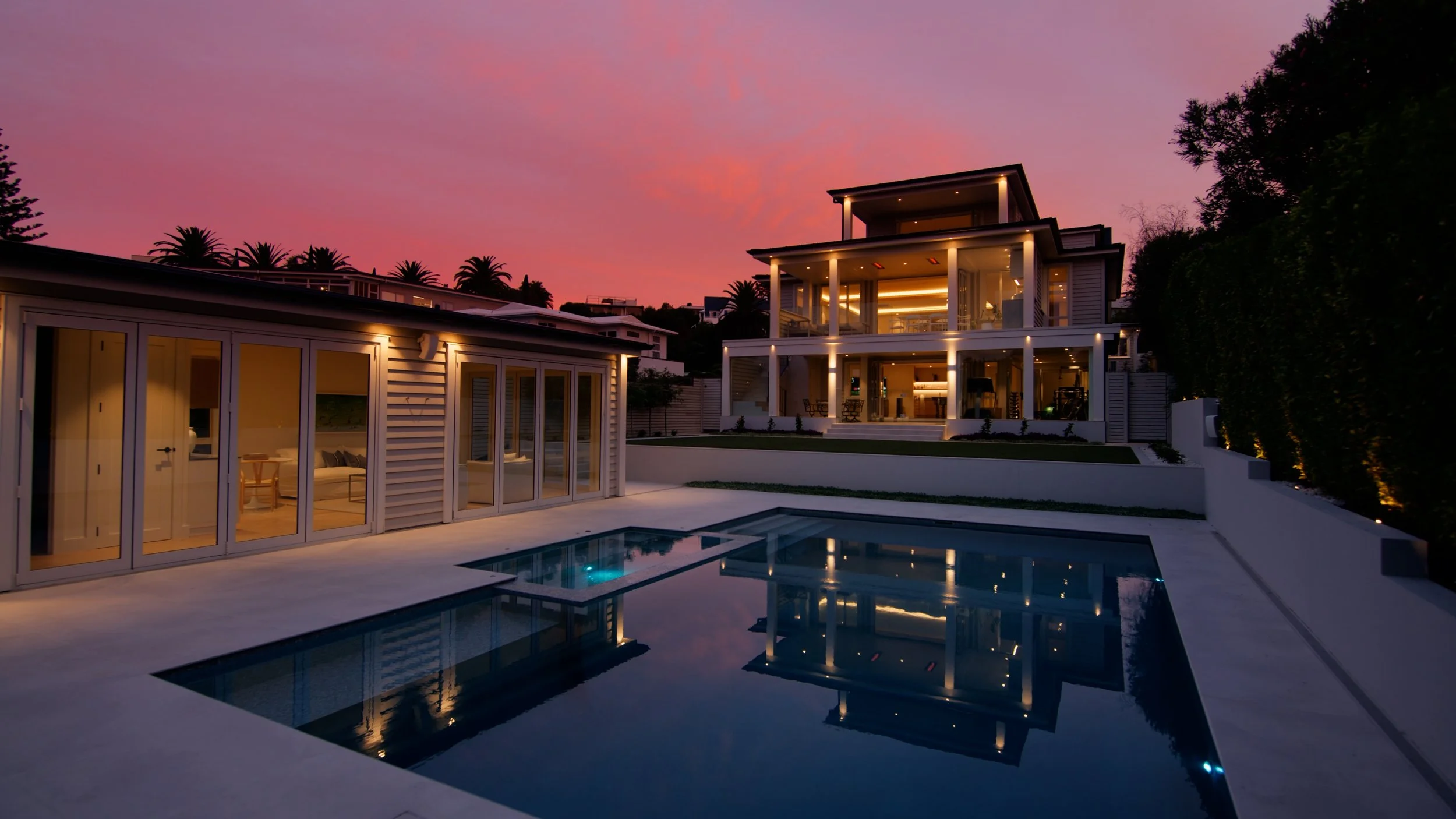 Luxury coastal estate at twilight, St Heliers Auckland - illuminated pool terrace and north-facing architectural home with Rangitoto Island views, Eastern Bays