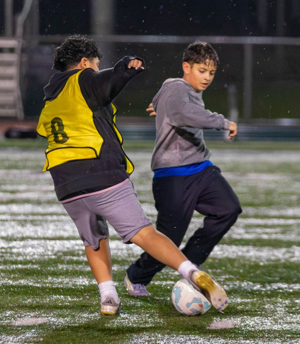 Two boys playing soccer on a wet field at night.