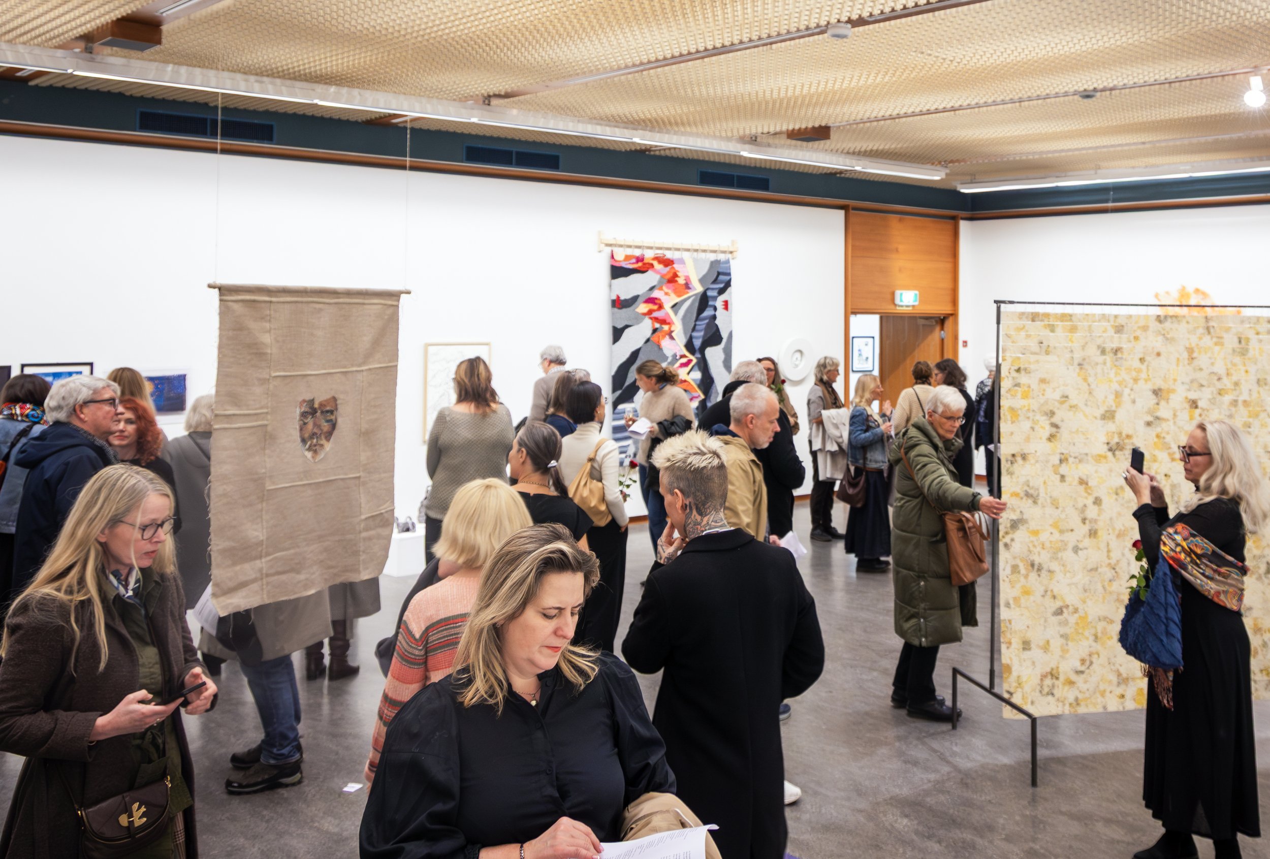 Mennesker på kunstutstilling i et galleri, mange ser på kunstverk og tar bilder.