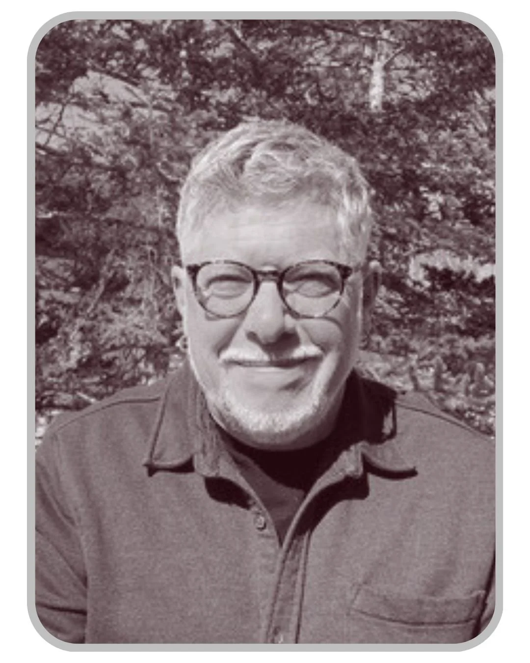 A smiling man with glasses and a beard outdoors in front of a tree.