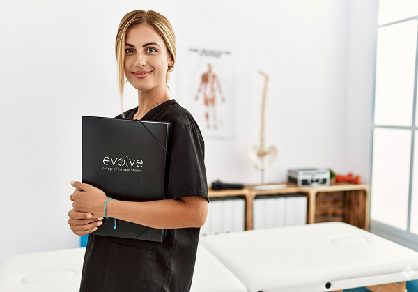 Image with RMT woman student holding a Evolve folder in a massage therapy room