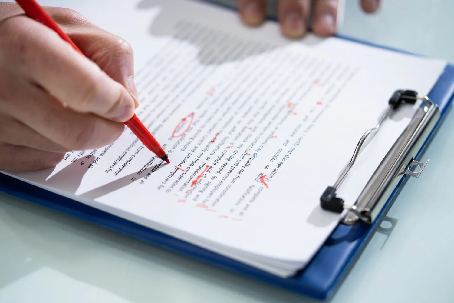A person reviewing a printed document on a clipboard, using a red pen with red markings and corrections.