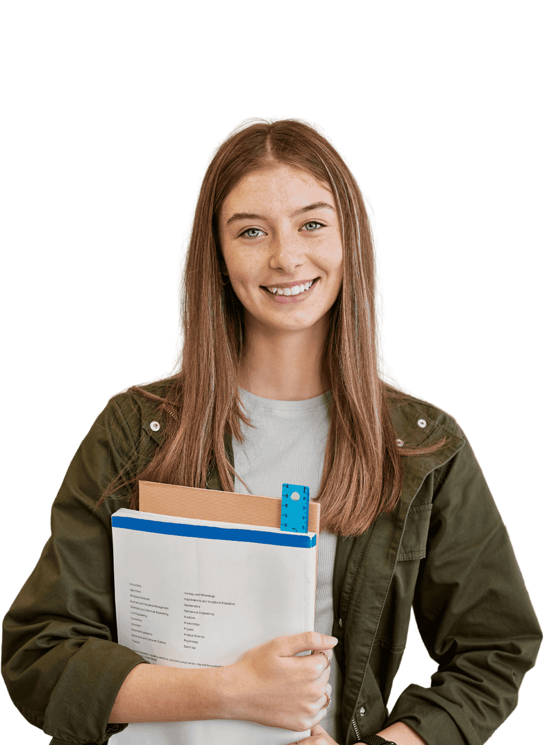 Smiling young woman with long reddish hair holding a stack of books and notebooks, dressed in a white shirt and olive-green jacket, standing against a black background.