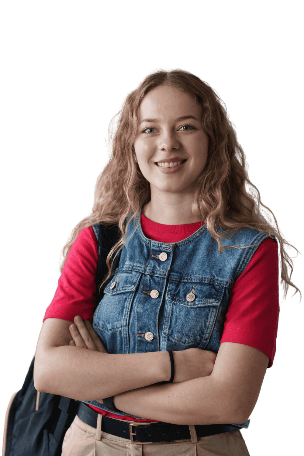 A young woman with long, curly blond hair, smiling and crossing her arms, wearing a red shirt, denim vest, khaki pants, and a black wristband, with a backpack over her shoulder.