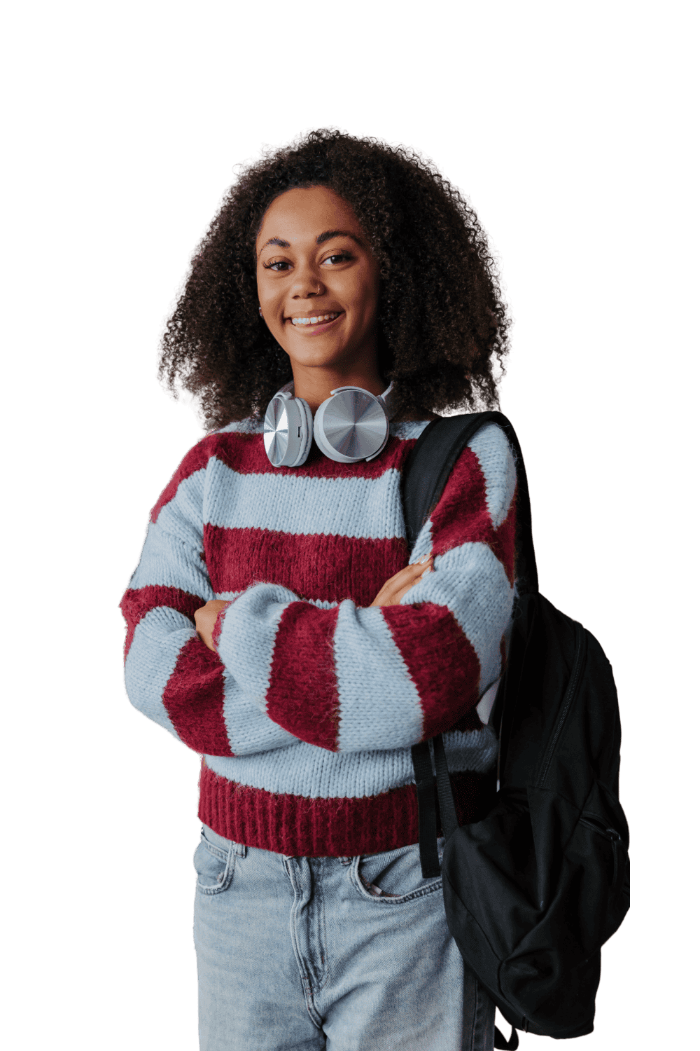 A young woman with curly hair smiling, wearing a red and light blue striped sweater, headphones around her neck, light blue jeans, and carrying a black backpack.