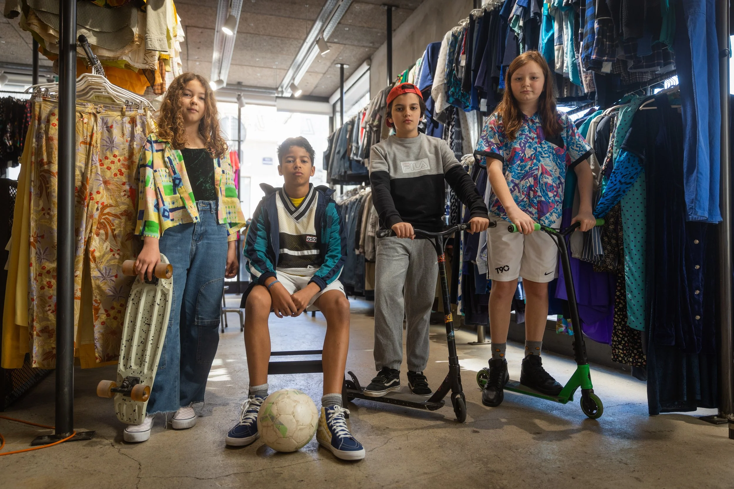 Cinq enfants posant avec des skateboards, un ballon de football et des trottinettes dans un magasin de vêtements