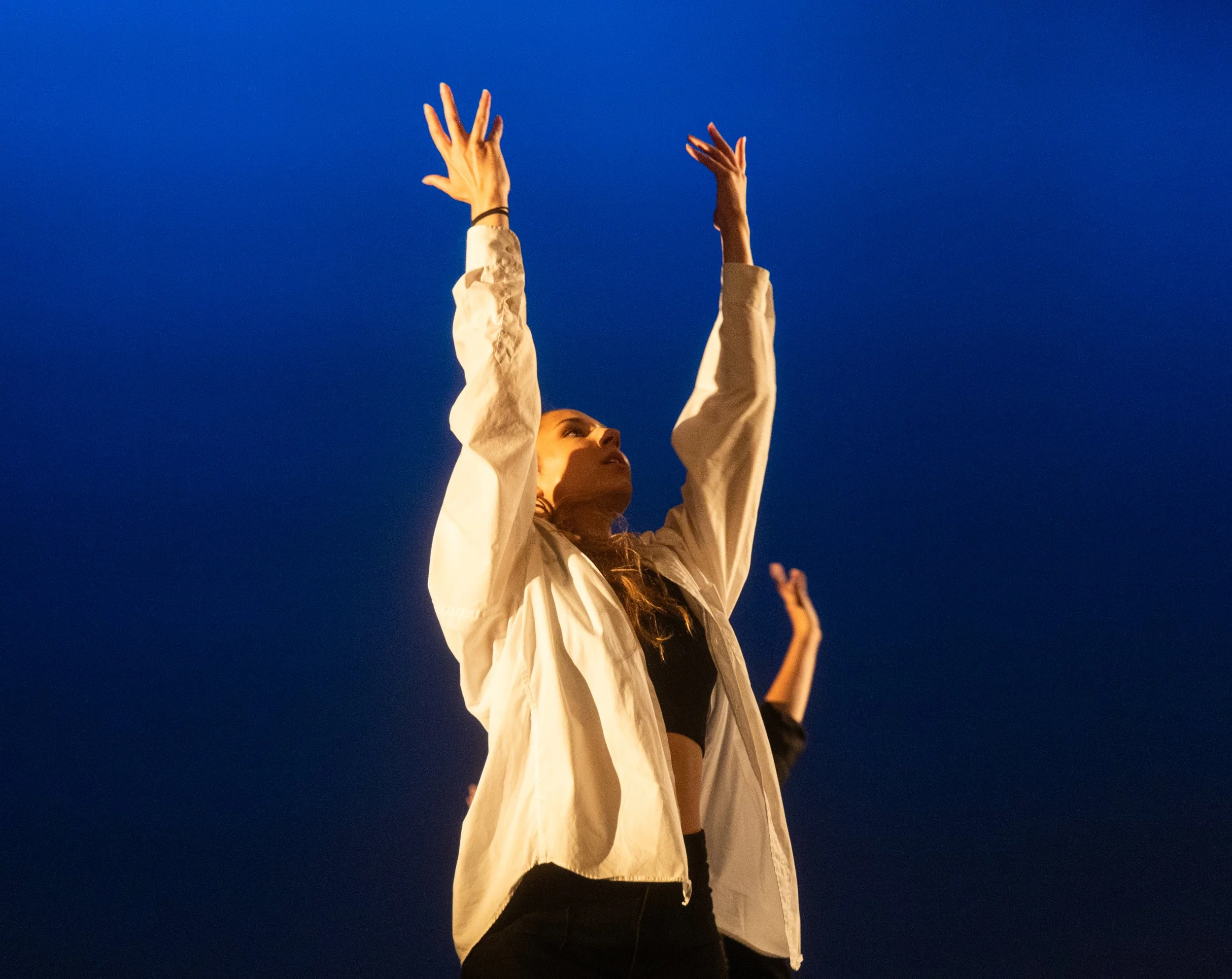 Une femme avec les bras levés vers le haut, portant une veste beige avec un fond de ciel bleu