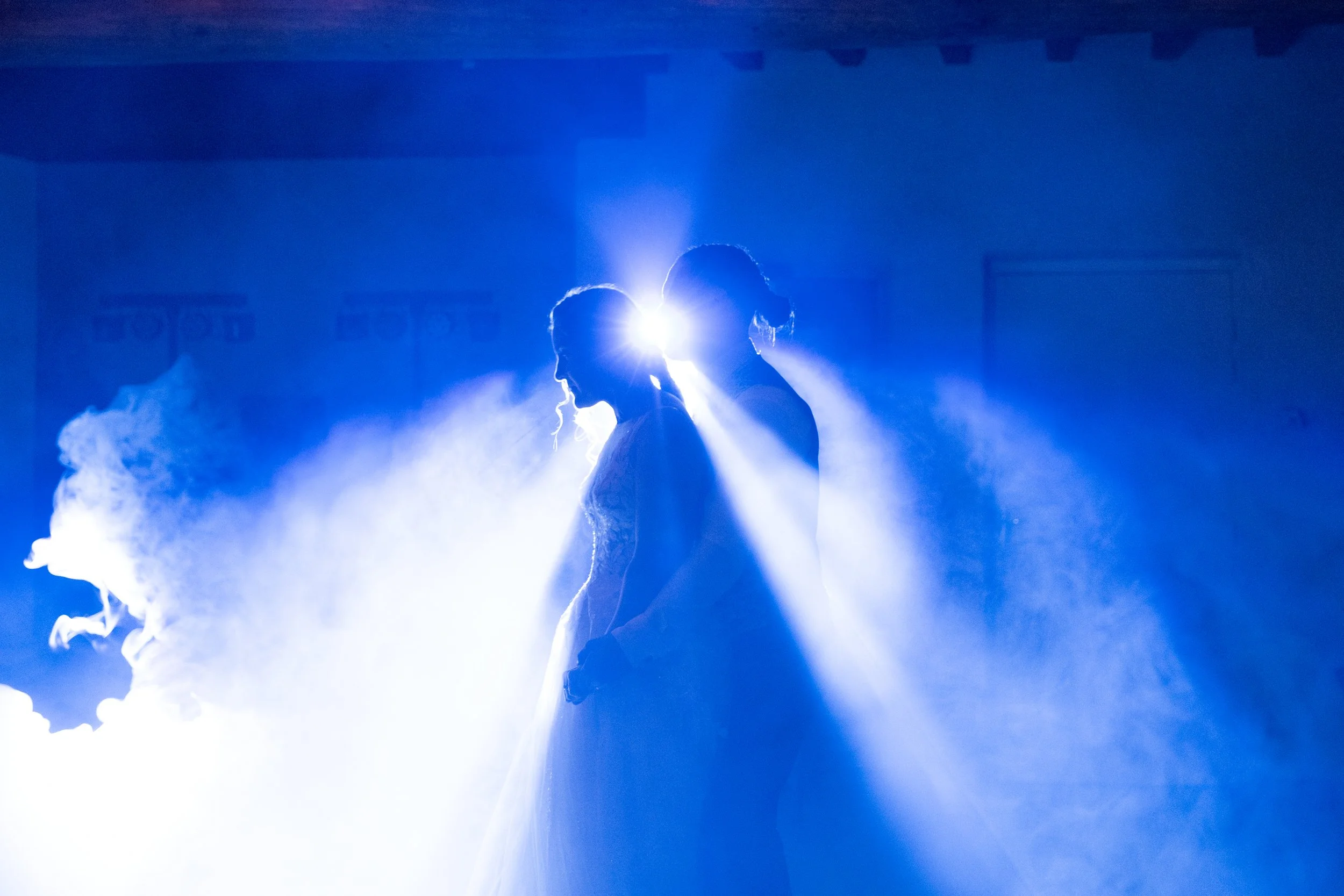 Un couple de mariés dansant lors de leur mariage sous un éclairage bleu avec de la fumée autour.